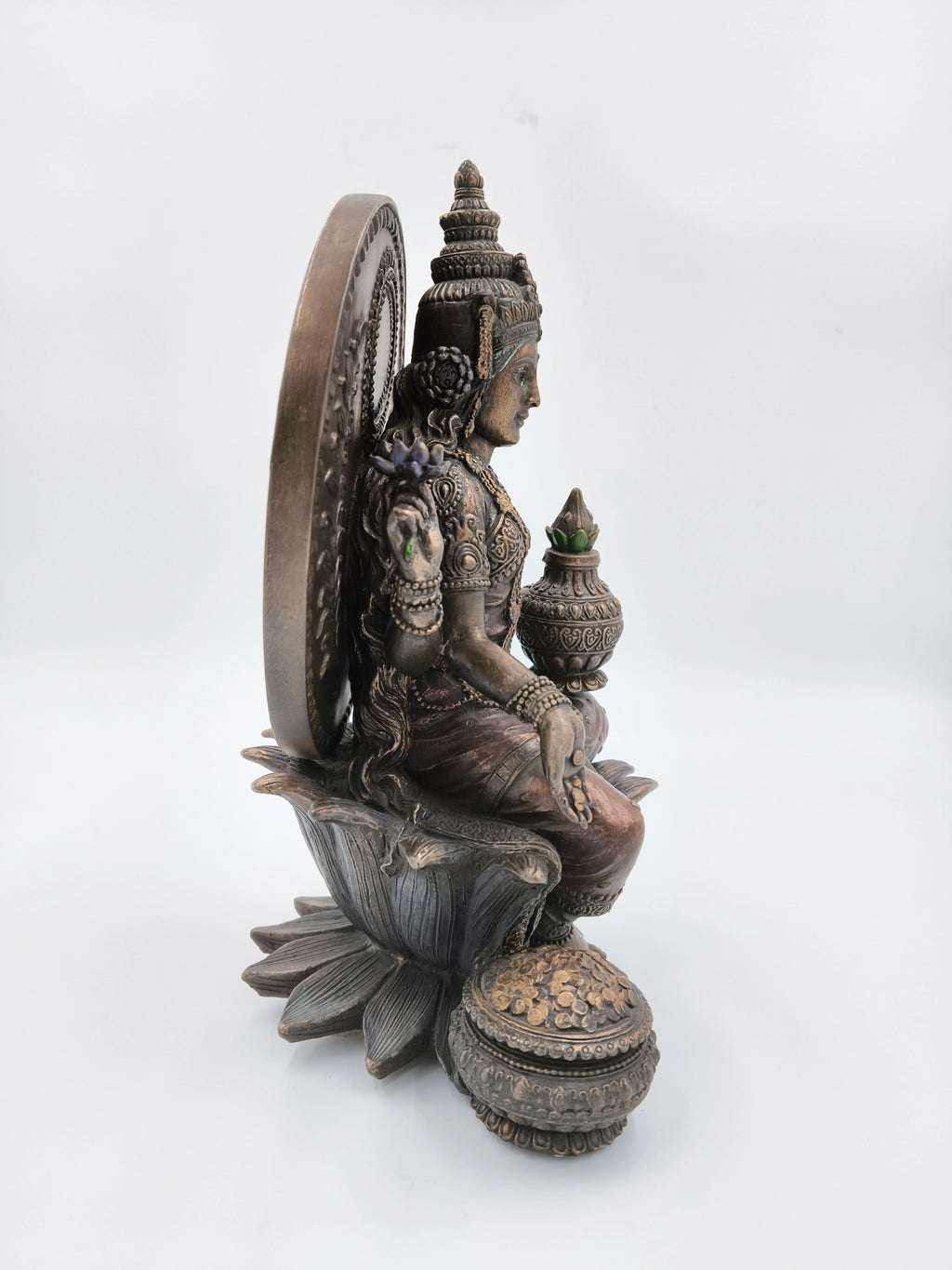 Side view of metallic fiber Lakshmi sculpture seated on lotus with pot and coins