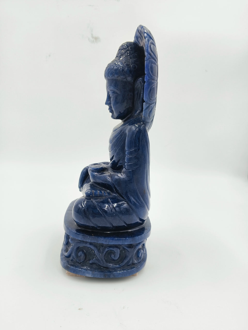 Side view of a blue jade Buddha sculpture seated on a carved pedestal