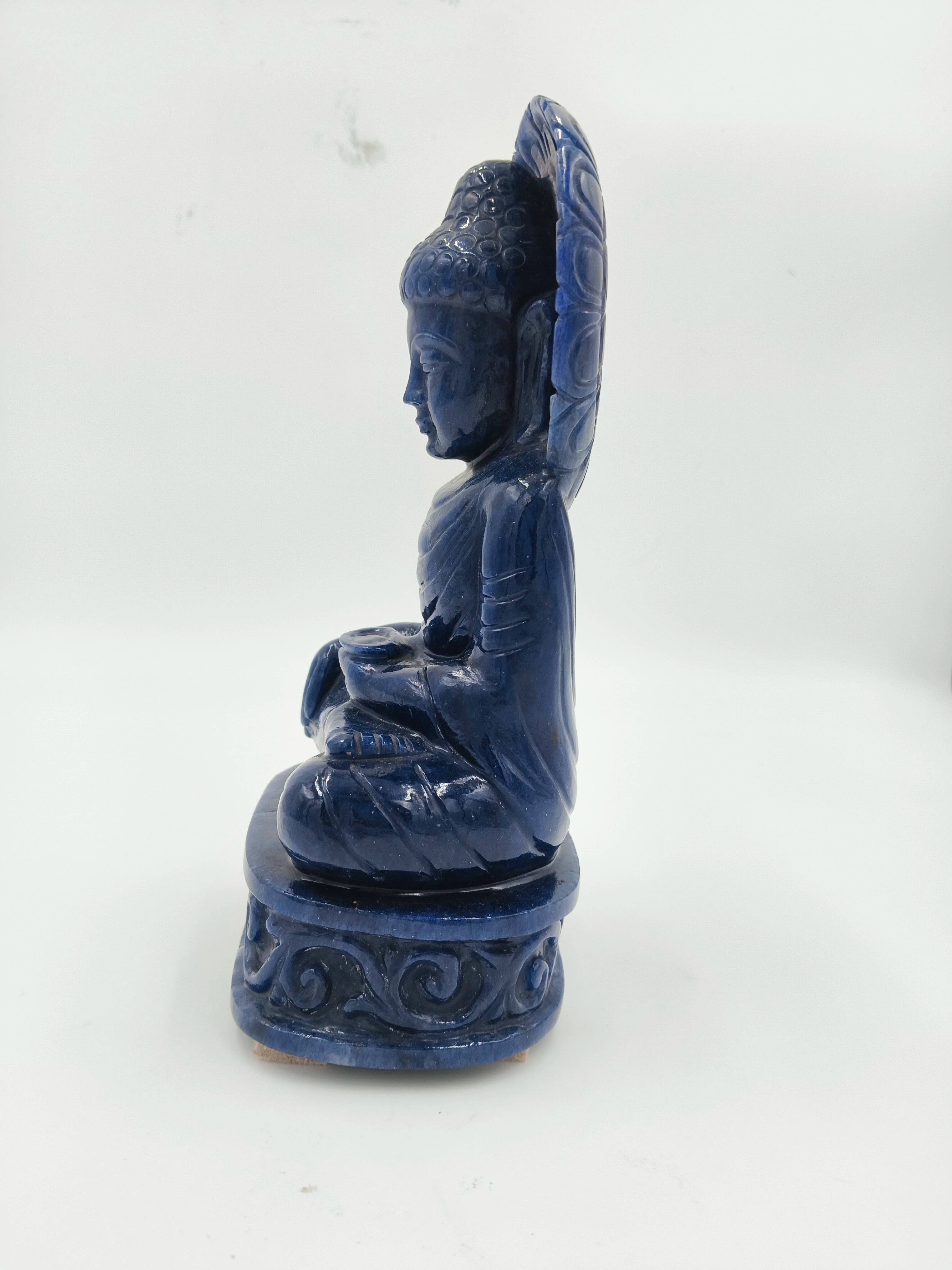 Side view of a blue jade Buddha sculpture seated on a carved pedestal