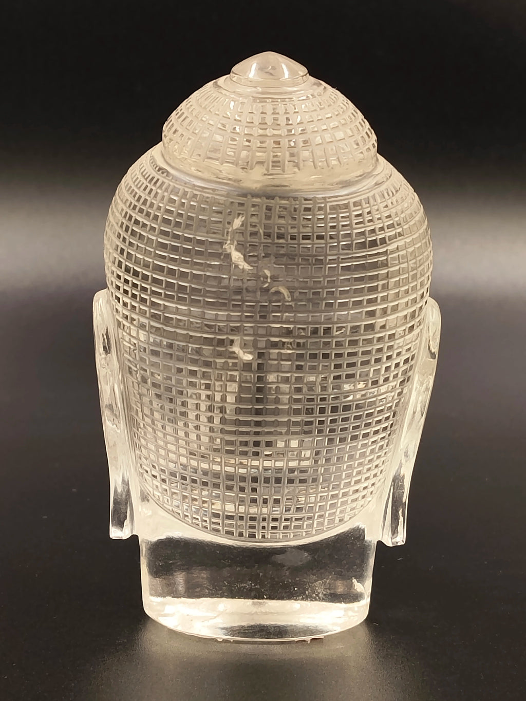 Rear view of a clear crystal Buddha head sculpture with textured surface