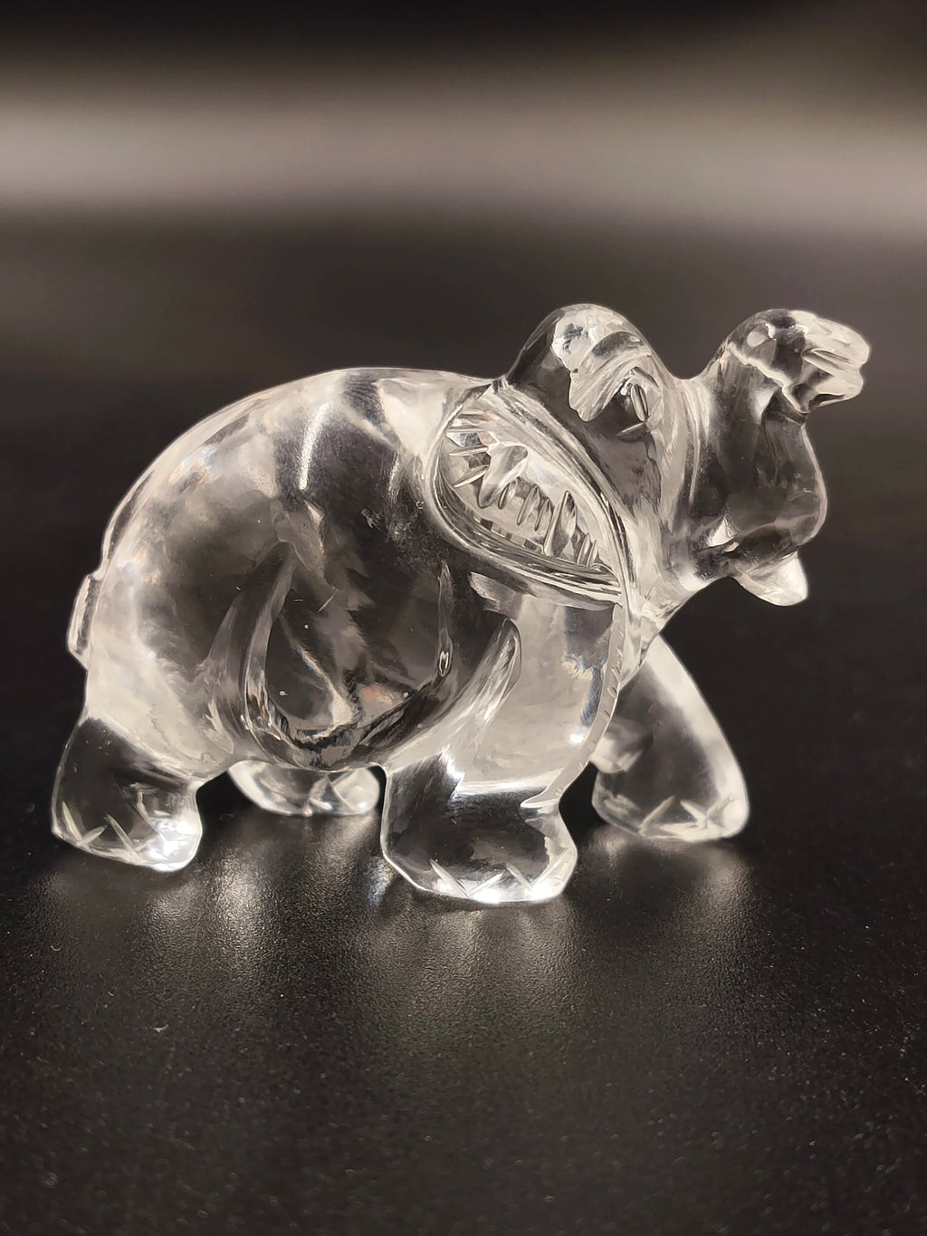 Clear crystal elephant figurine sculpture on black surface, side view