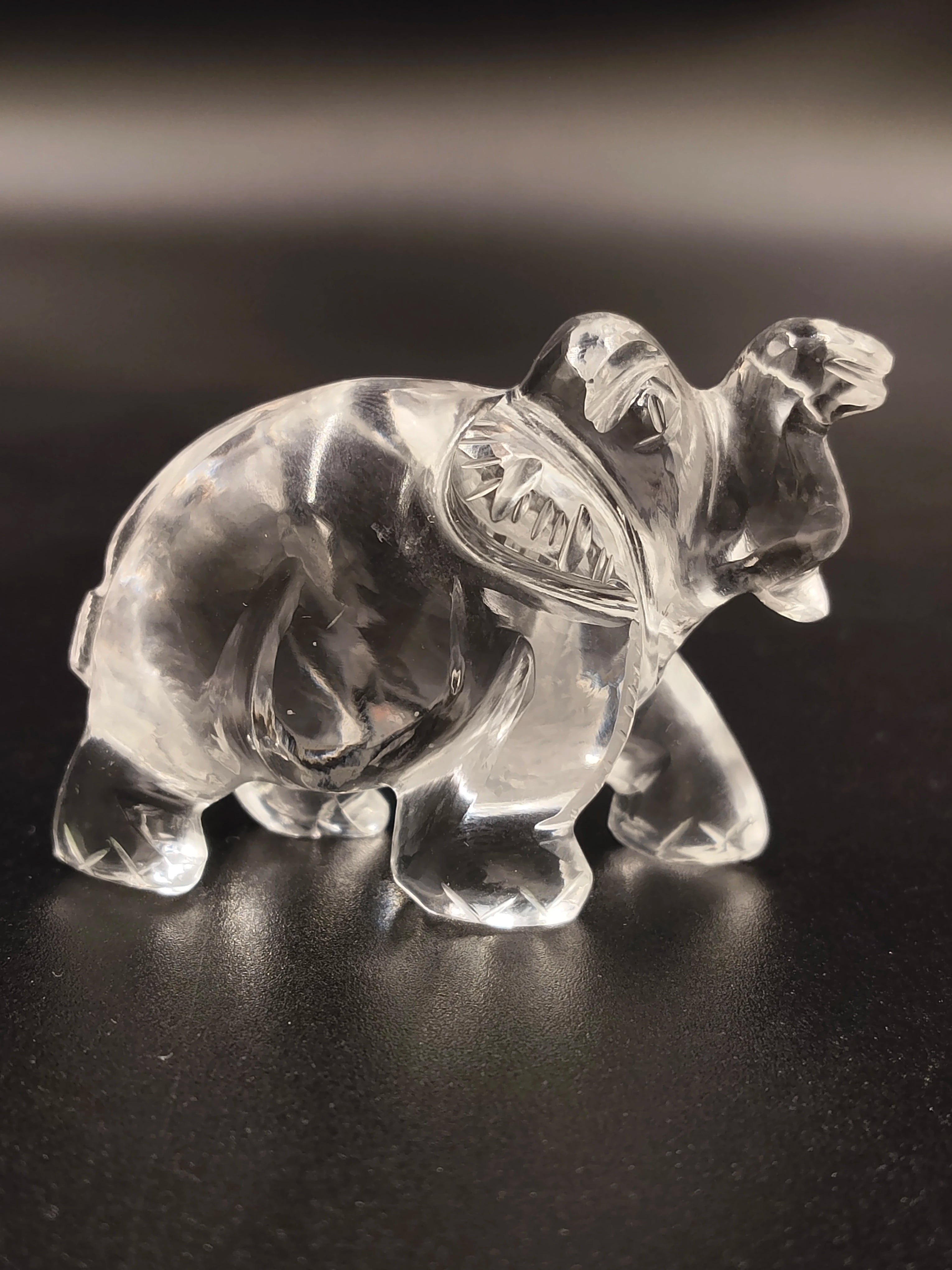 Clear crystal elephant figurine sculpture on black surface, side view