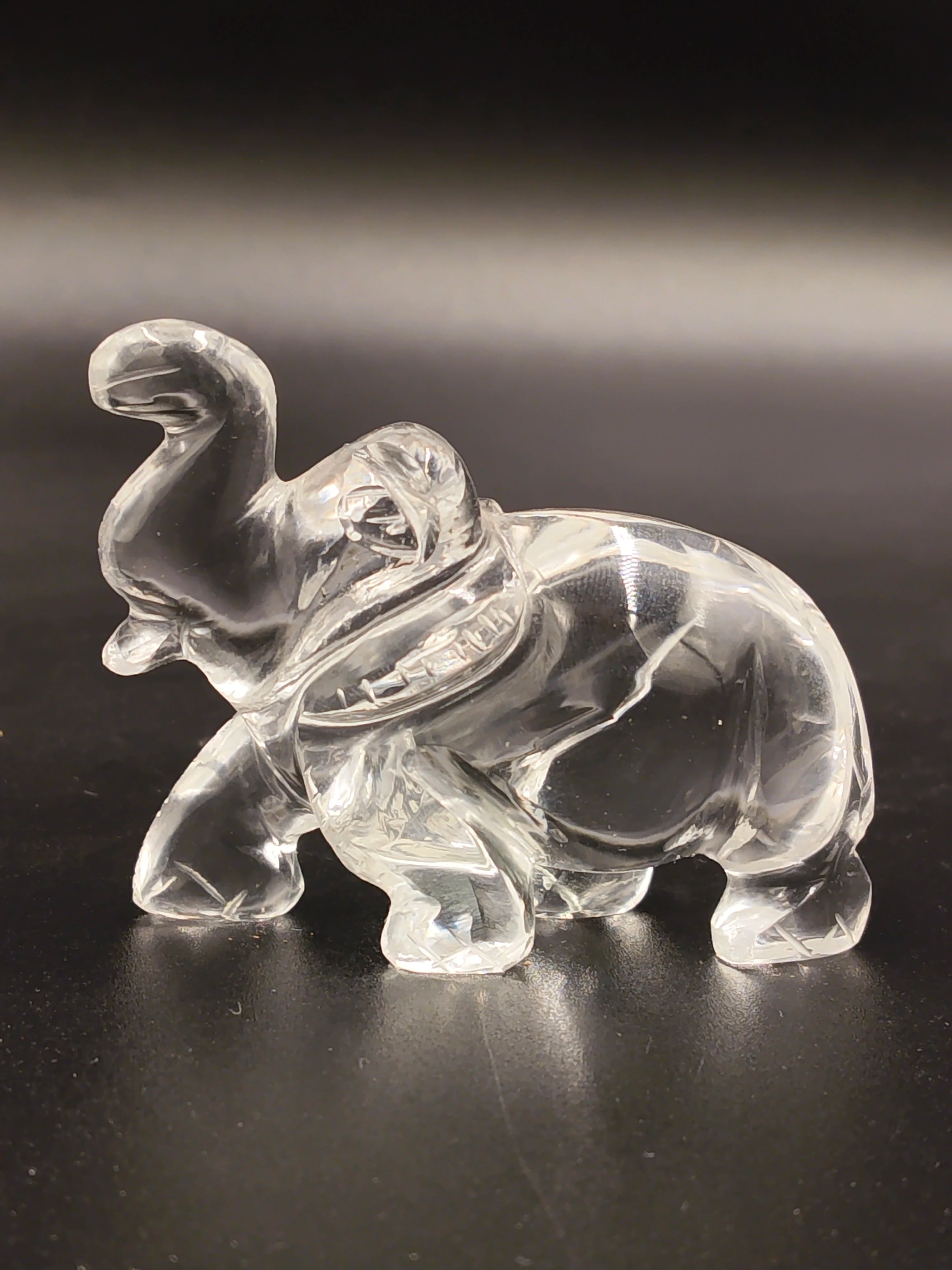 Clear crystal elephant figurine sculpture with raised trunk on black background