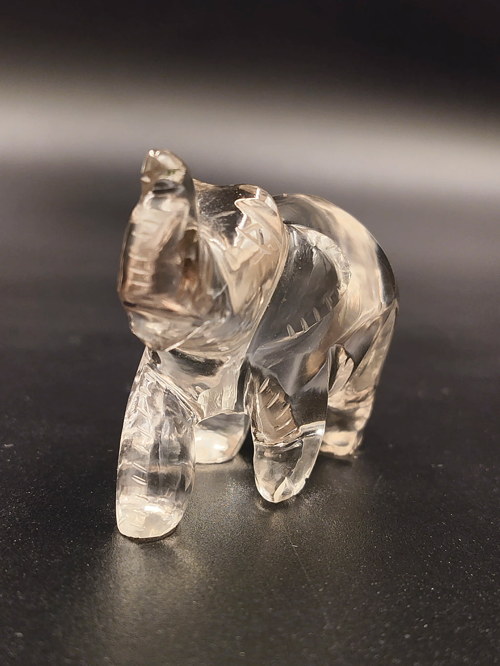 Clear crystal elephant figurine sculpture on dark surface, front side view
