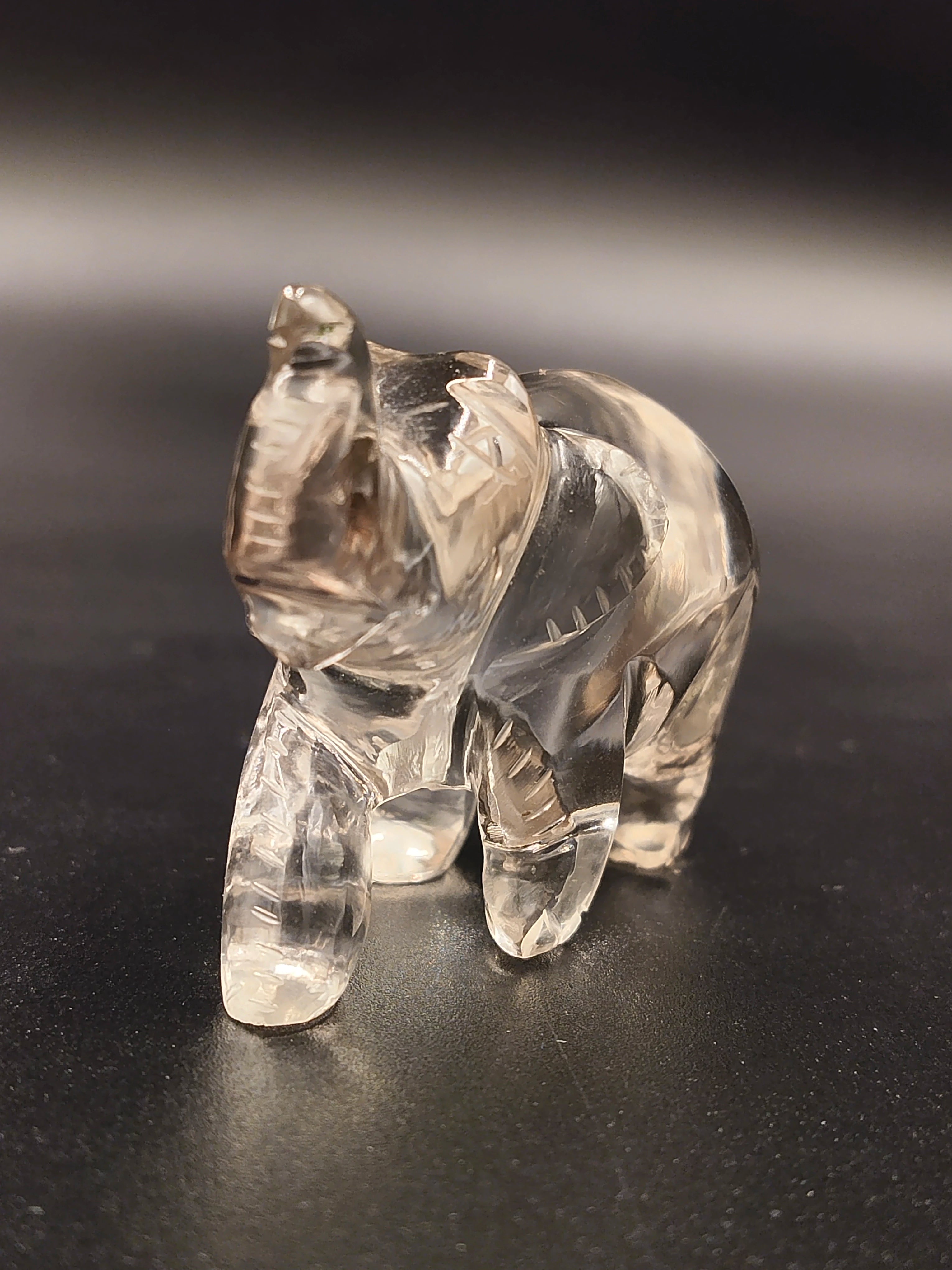 Clear crystal elephant figurine sculpture on dark surface, front side view