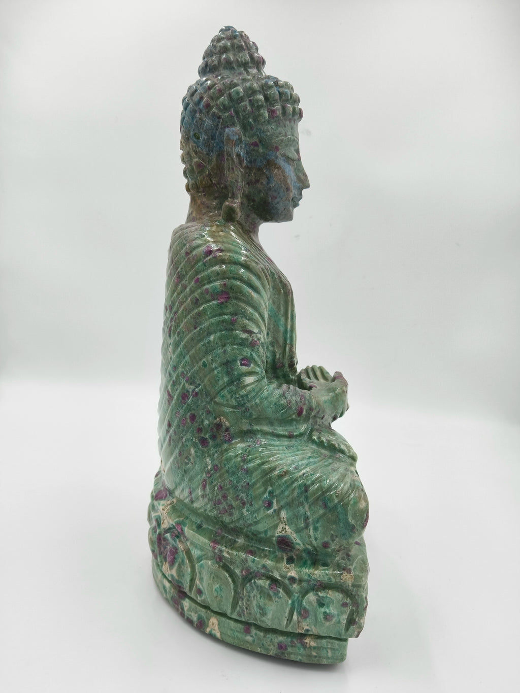 Side view of a green and purple Rubylite Buddha statue sitting in meditation
