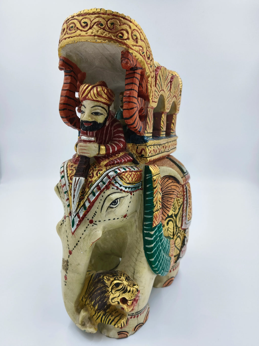 Side view of serpentine elephant ambari sculpture with painted rider and lion figurine
