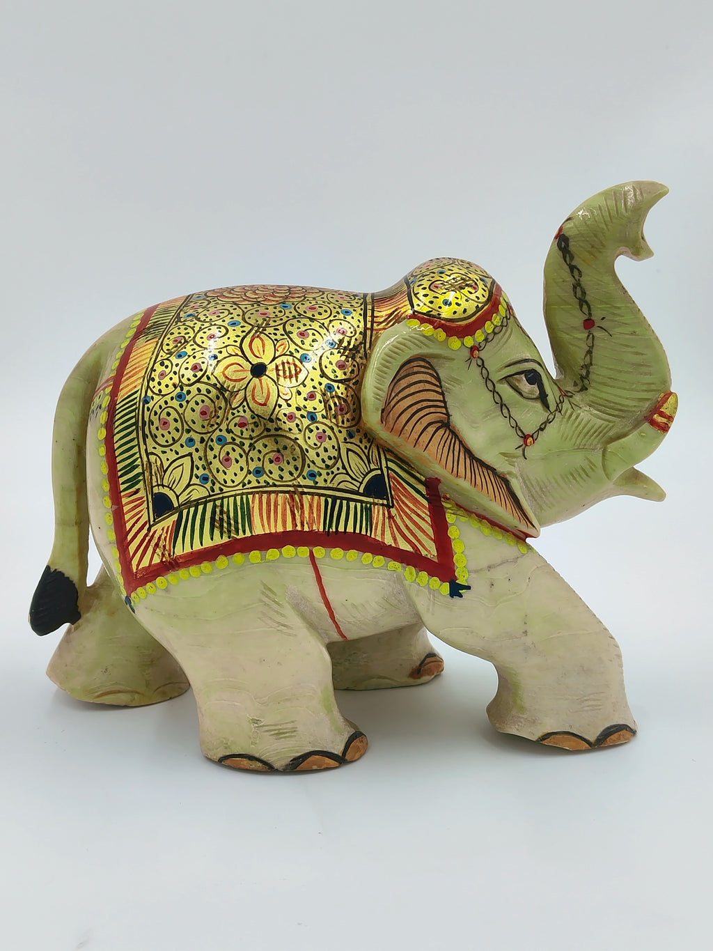 Serpentine elephant sculpture with golden floral decorations and raised trunk