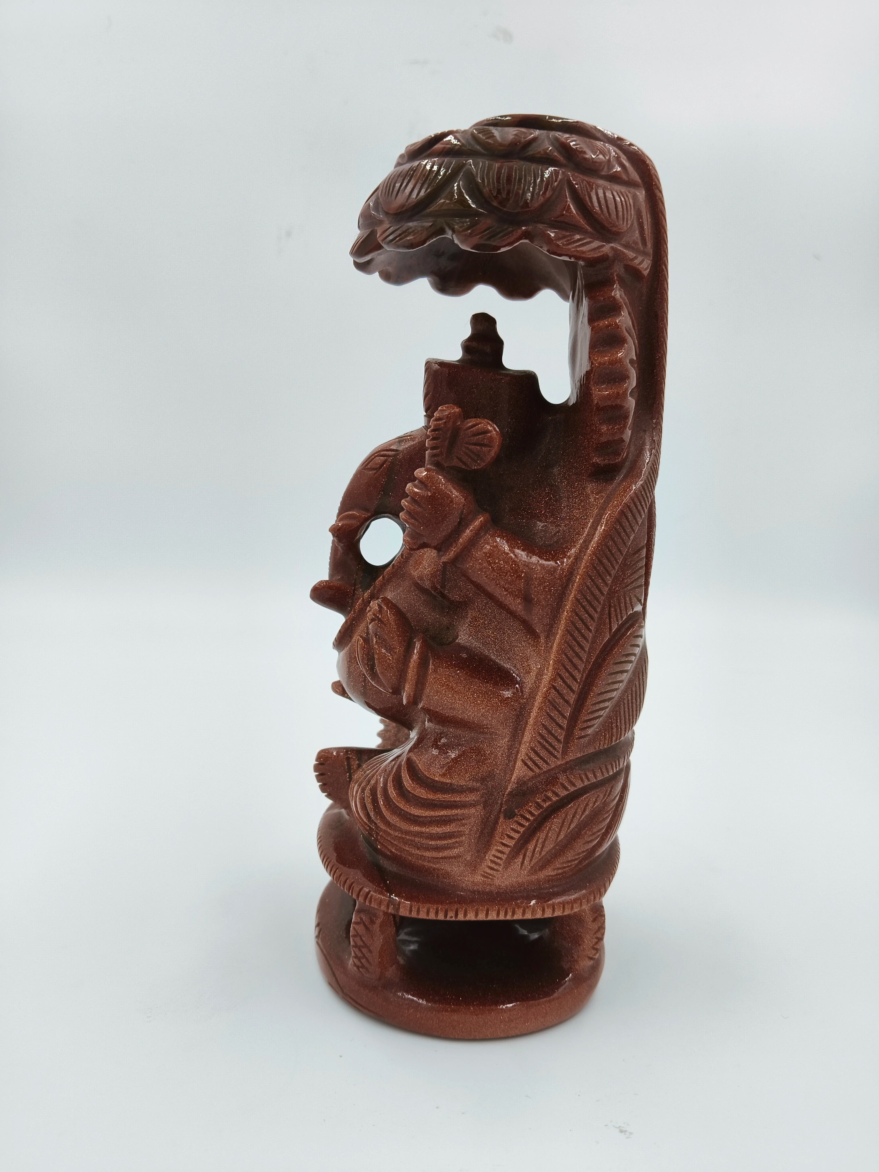 Carved sunstone statue of Ganesh holding an umbrella in side view