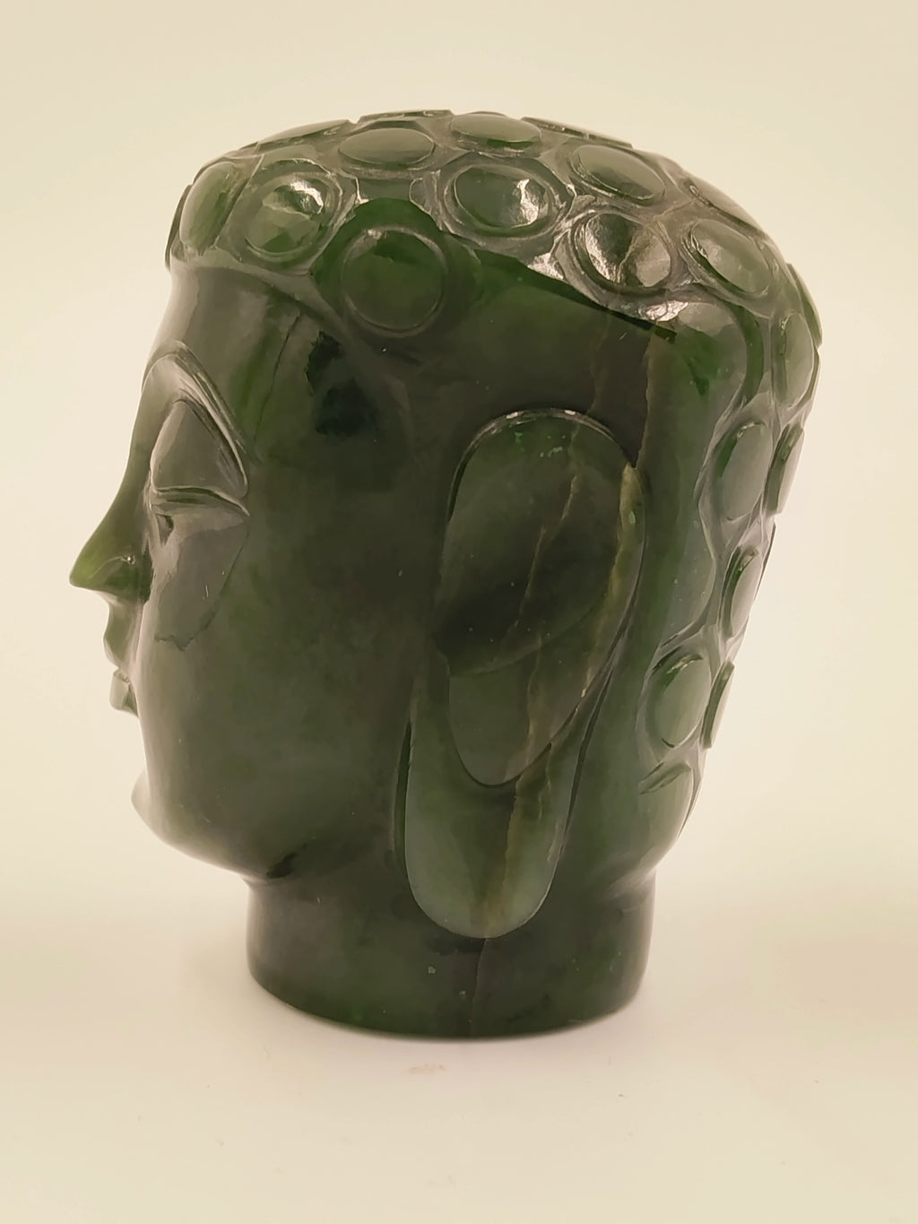 Side view of small jade Buddha head sculpture with detailed hair curls