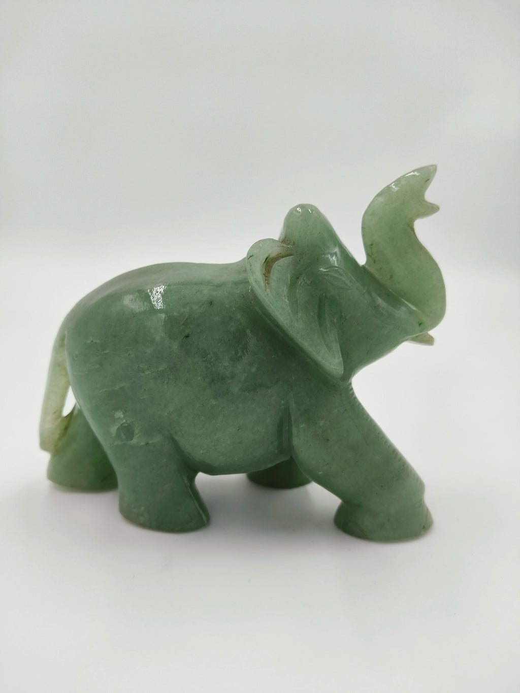 Small green jade elephant figurine with raised trunk in side view