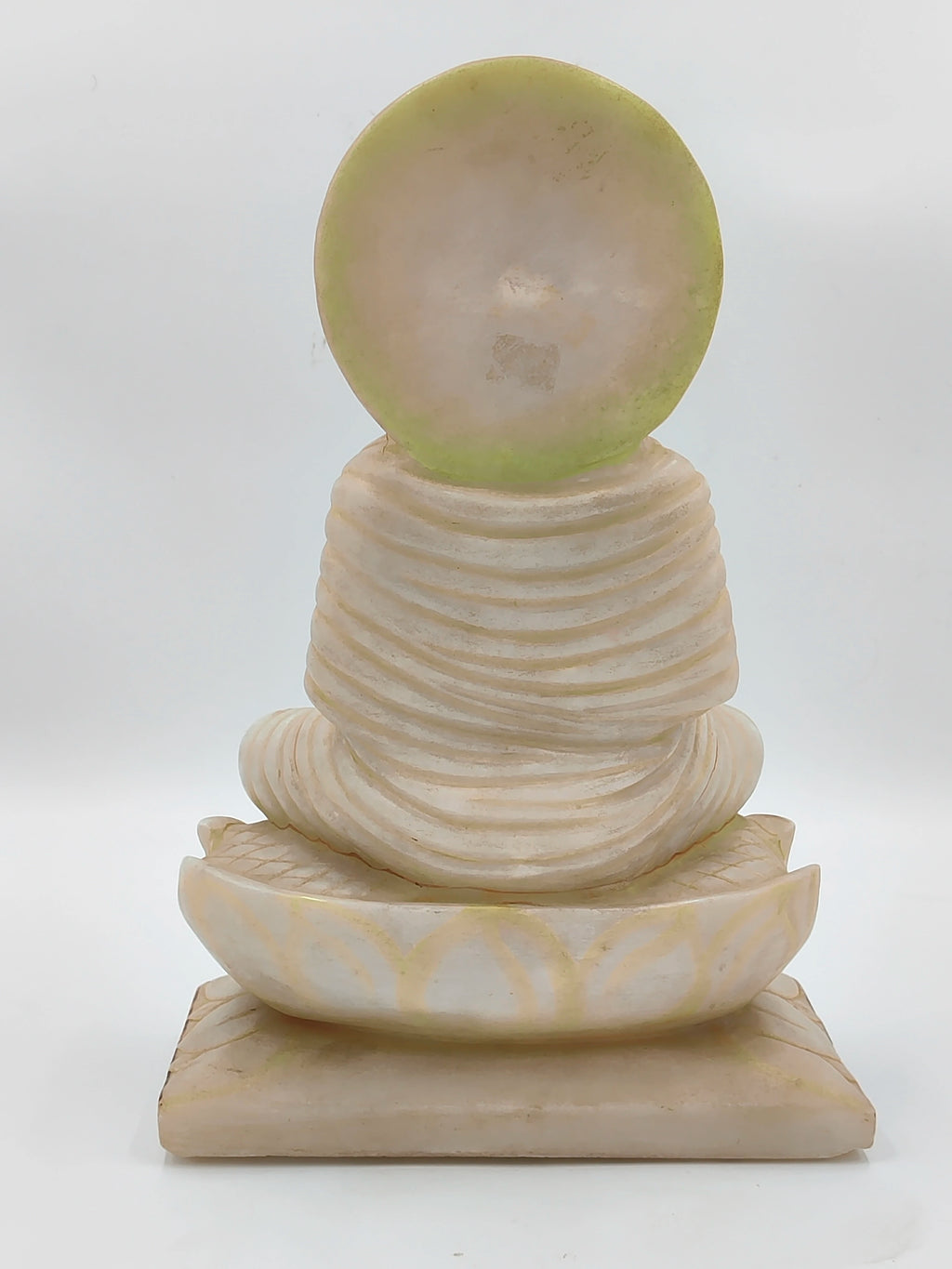 Back view of white marble Buddha sculpture seated on lotus base