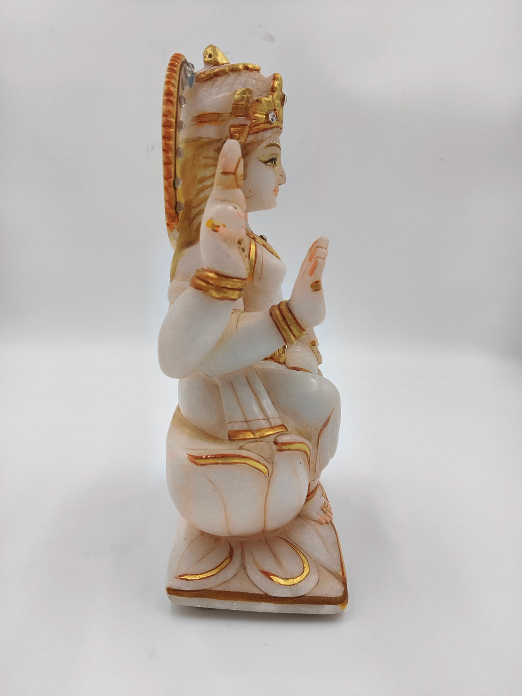 Side view of white marble Lakshmi statue with gold accents seated on lotus base