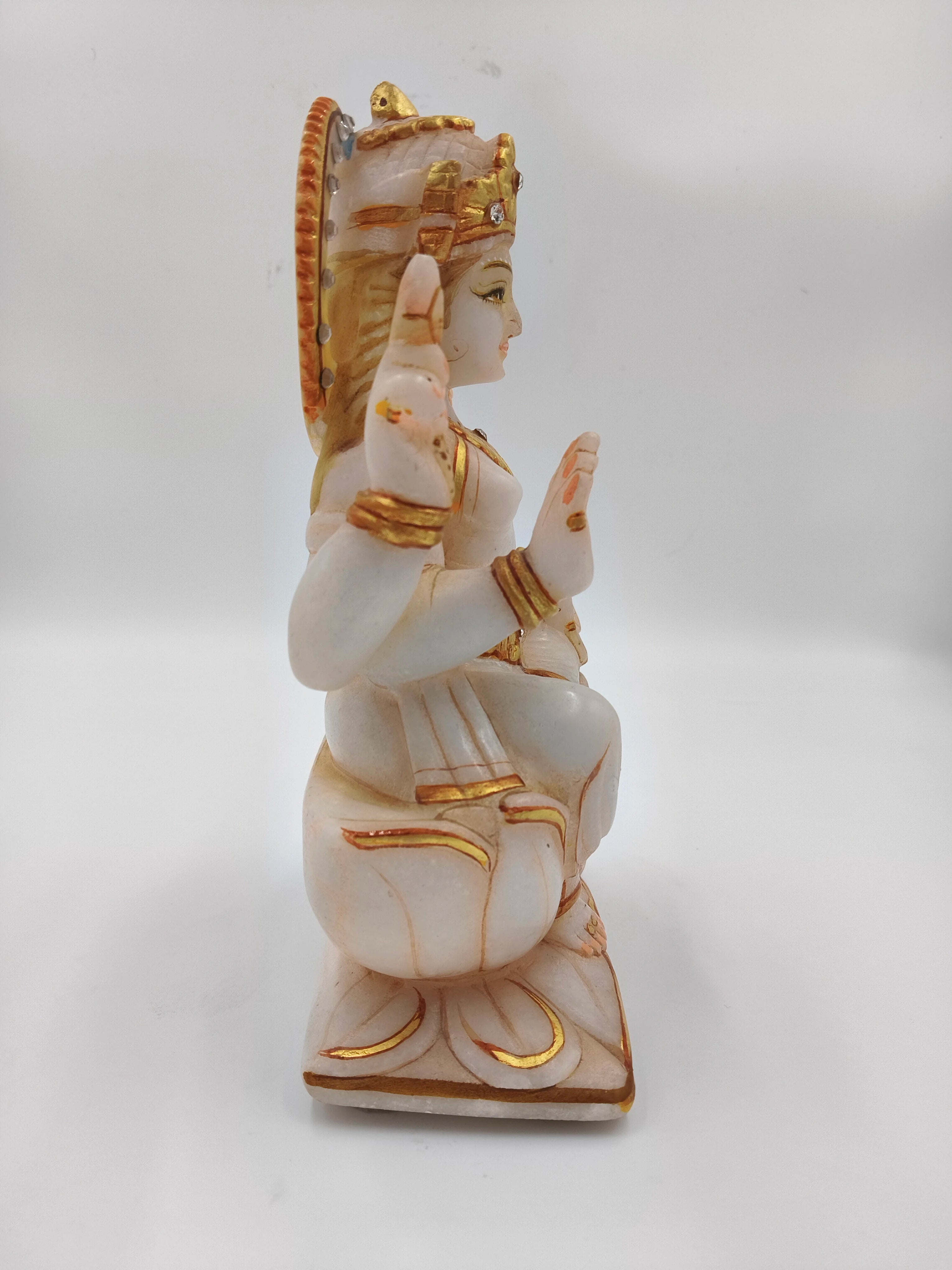 Side view of white marble Lakshmi statue with gold accents seated on lotus base