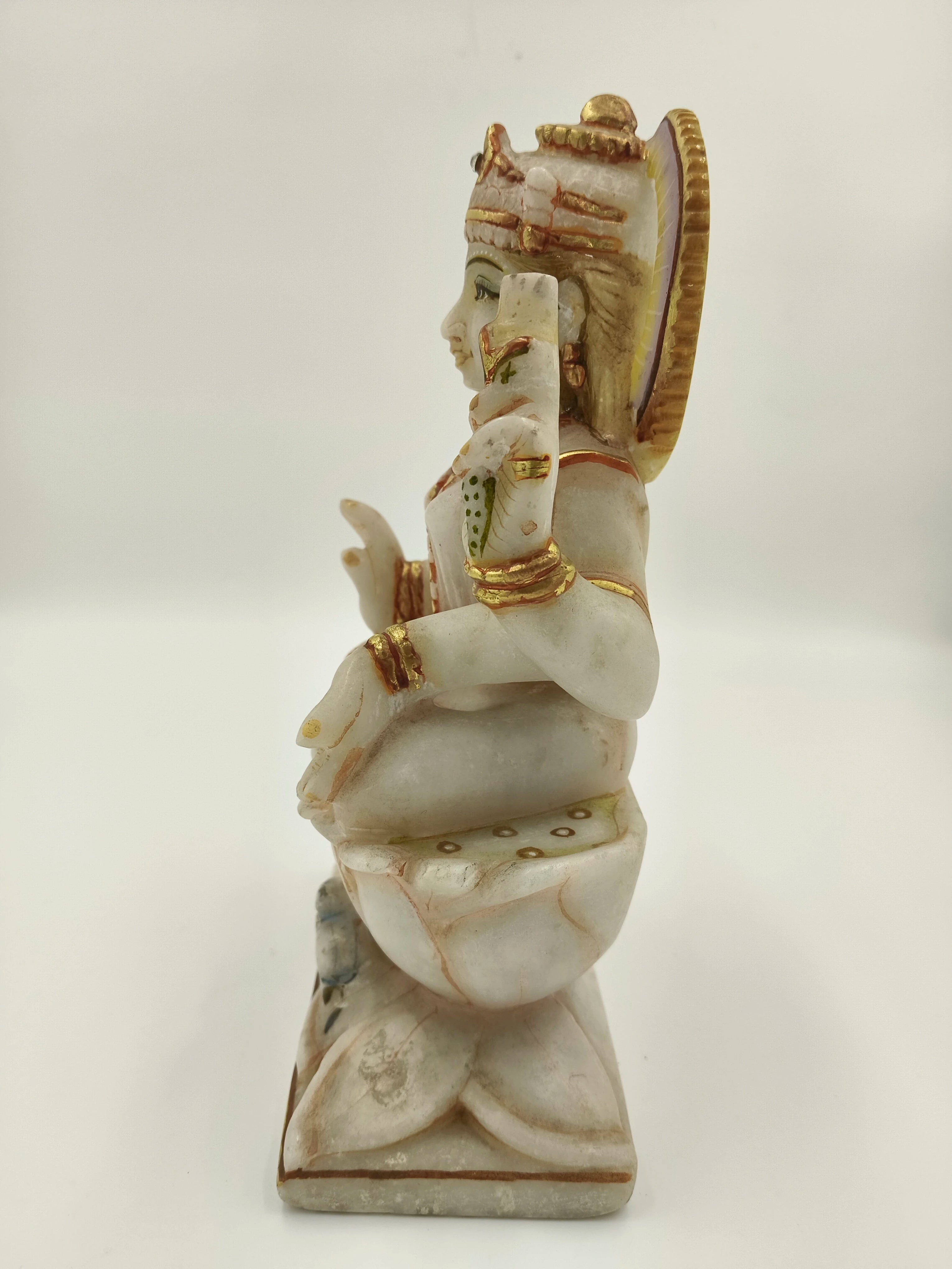 Side view of marble Lakshmi statue with gold and green accents seated on lotus