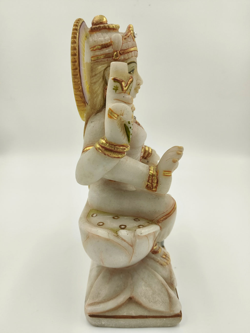 Side view of a marble statue of Lakshmi seated on a lotus flower decorated with gold accents