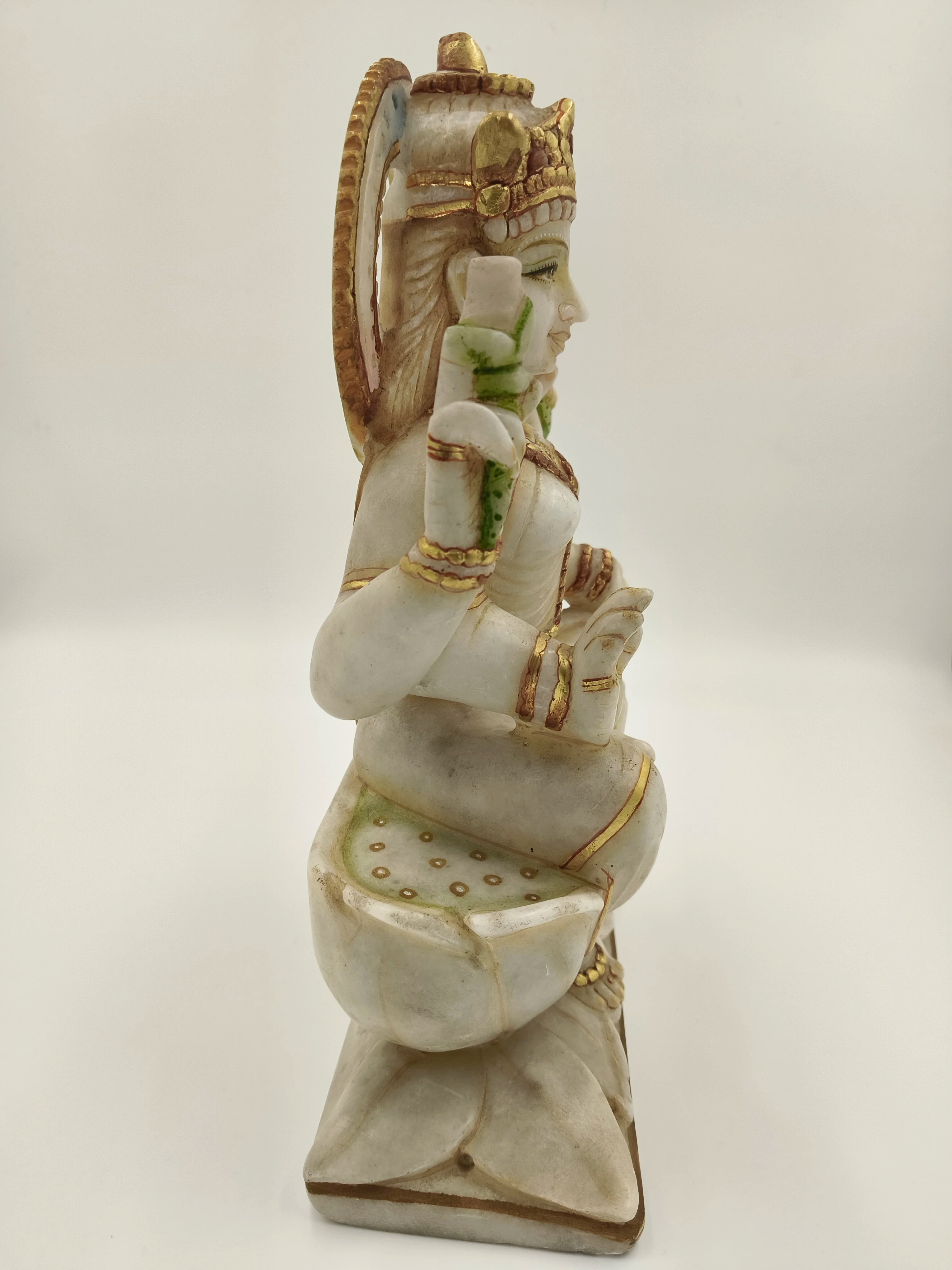 Side view of a large white marble Lakshmi statue with gold and green accents