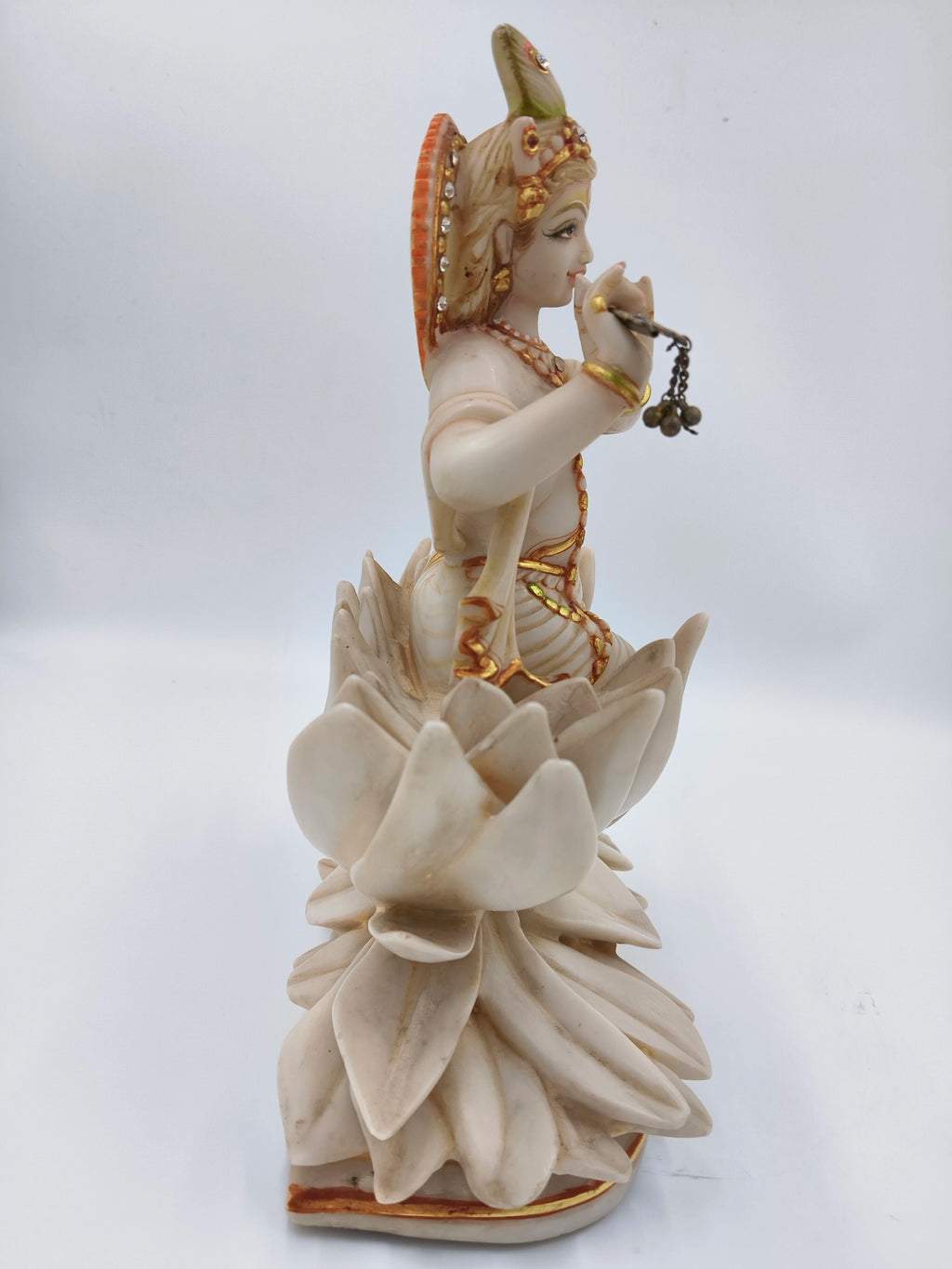 Side view of marble dust Krishna sculpture sitting on lotus with flute