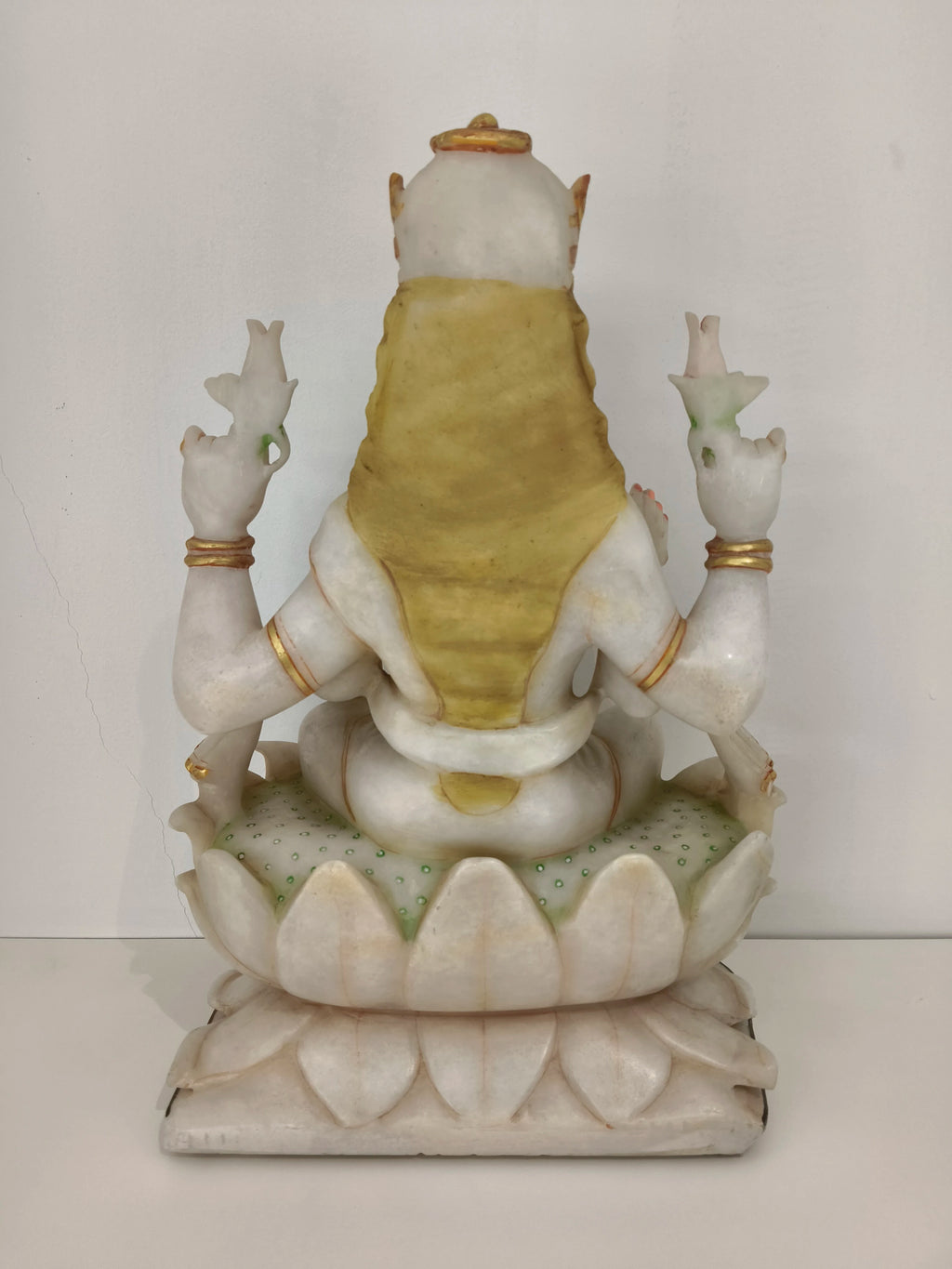Back view of large white marble Lakshmi statue seated on lotus base with gold accents