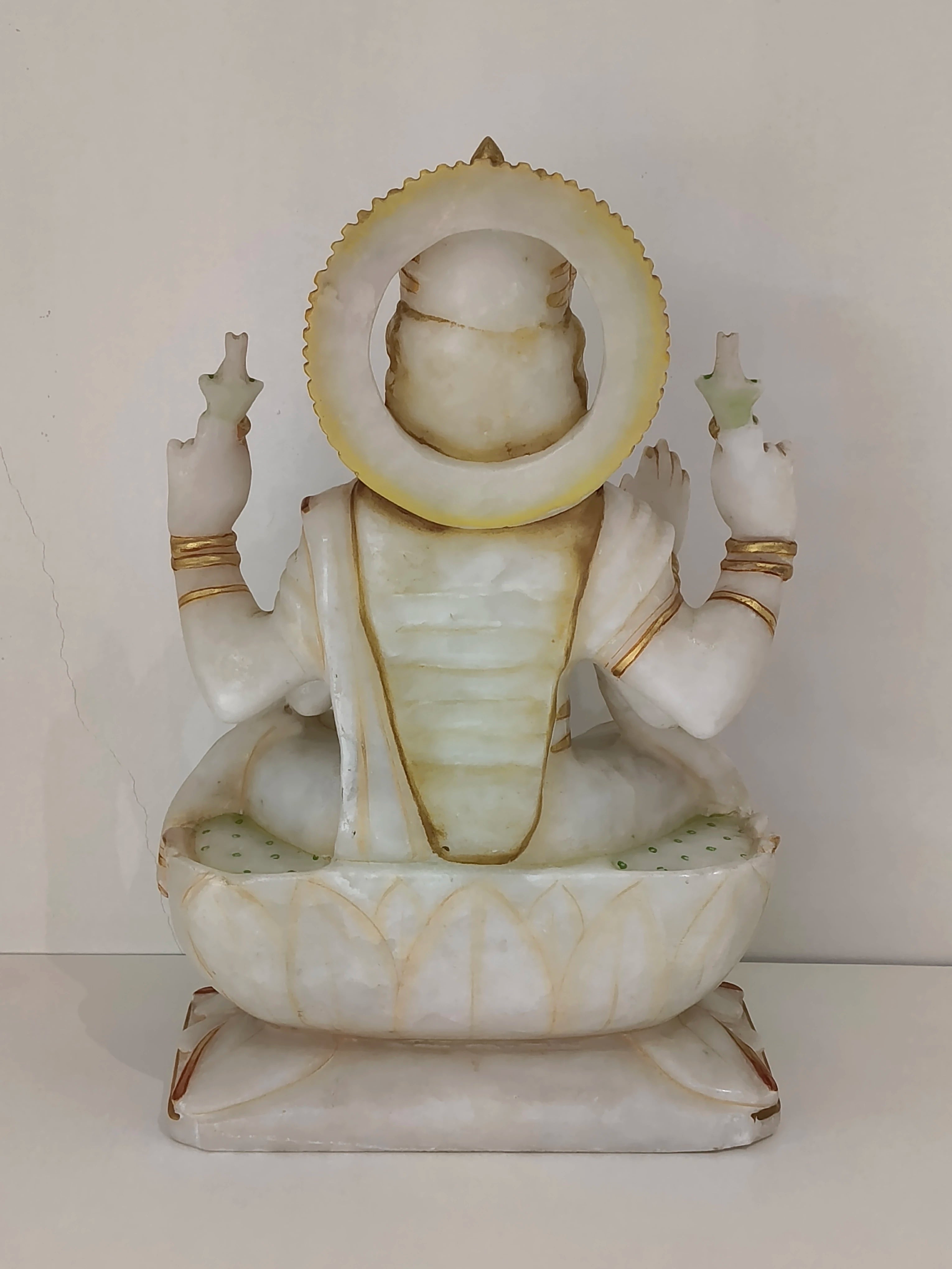 Back view of large marble statue of Lakshmi seated on lotus base with gold accents