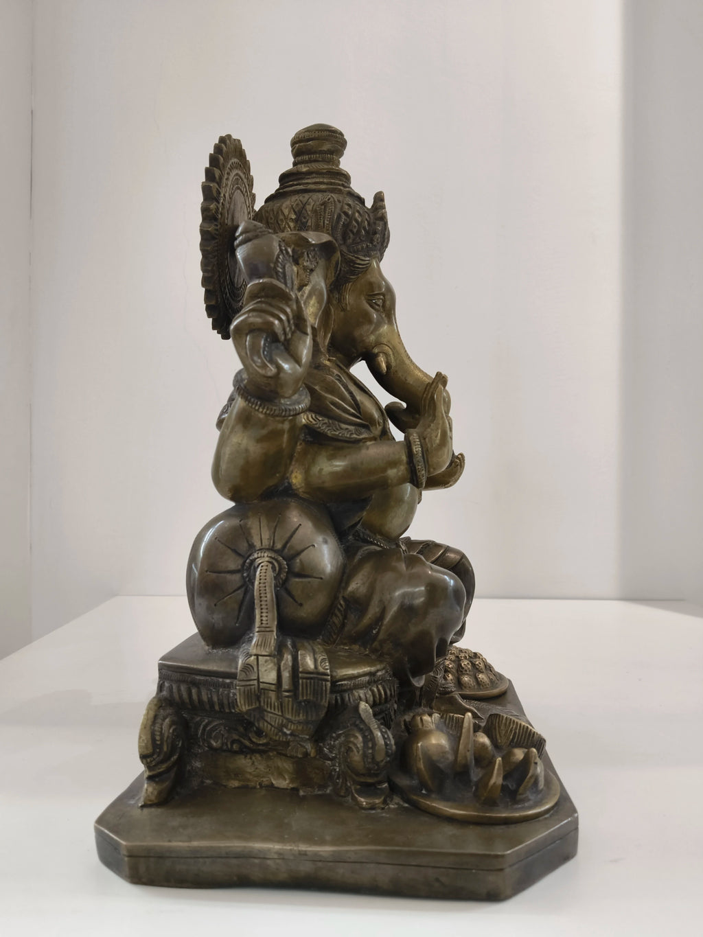 Side view of large brass Ganesh statue seated on a decorated pedestal