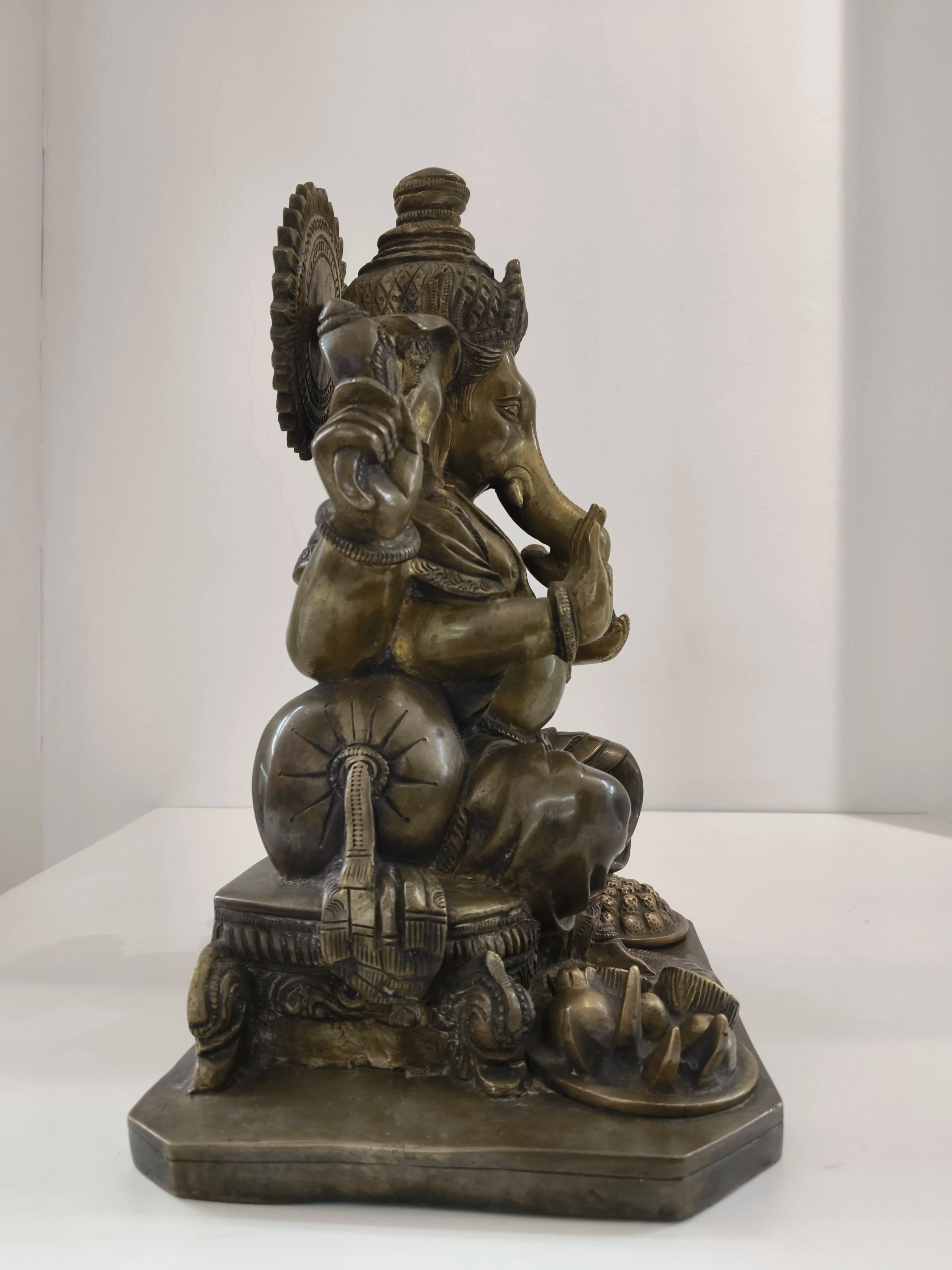 Side view of large brass Ganesh statue seated on a decorated pedestal