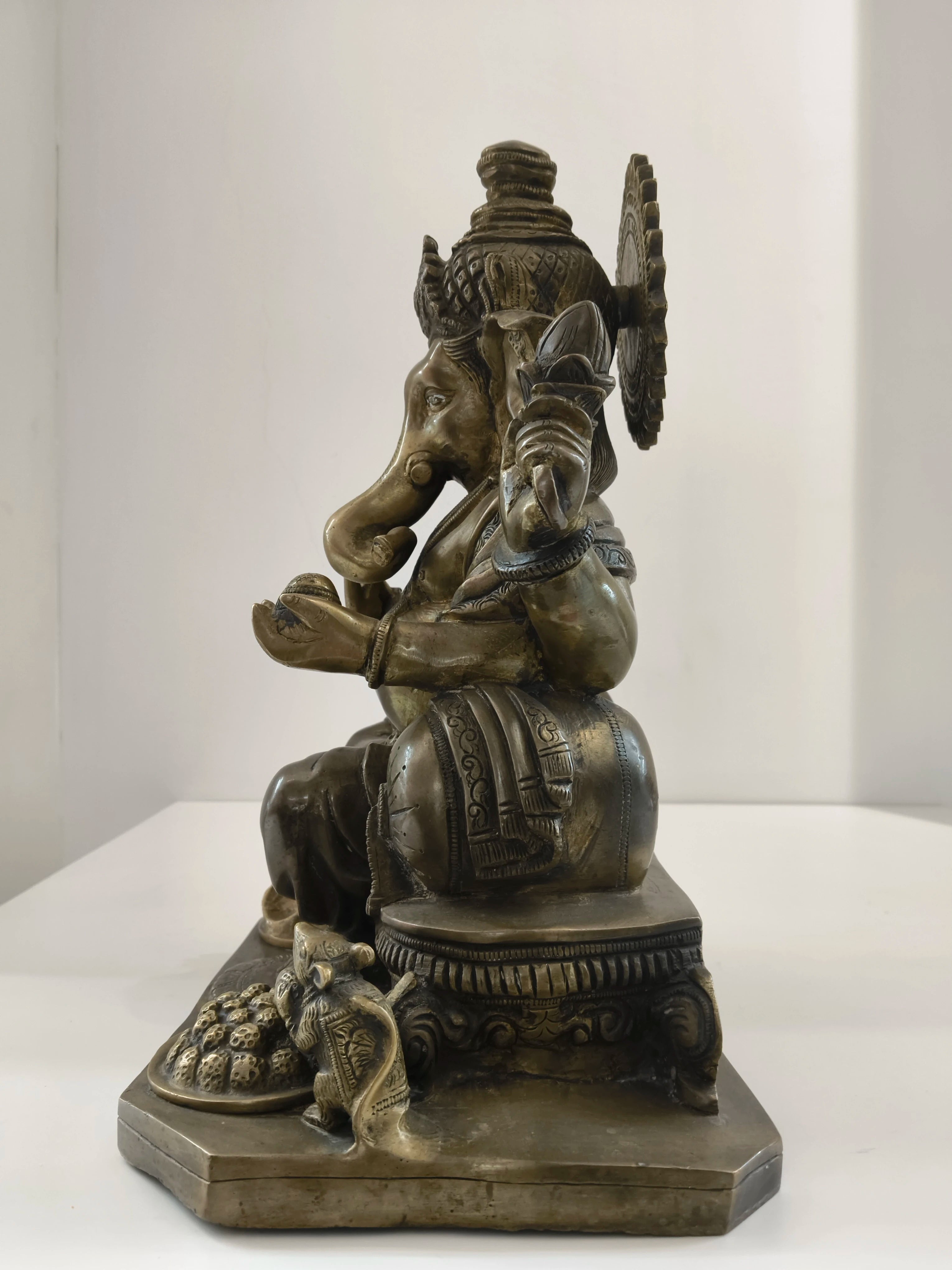 Side view of large brass Ganesh statue seated on a decorated base