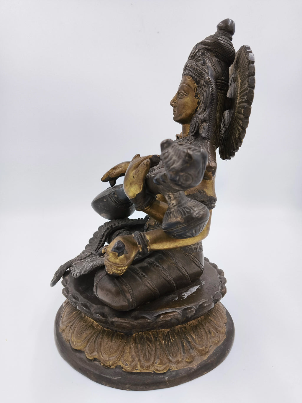Side view of brass Saraswathi statue seated on a lotus base