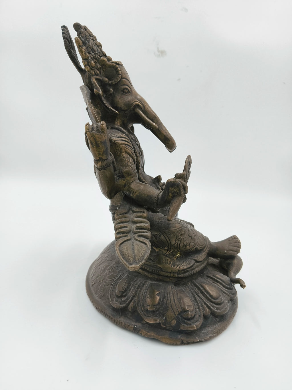 Side view of a brass Ganesh statue seated on a decorative base