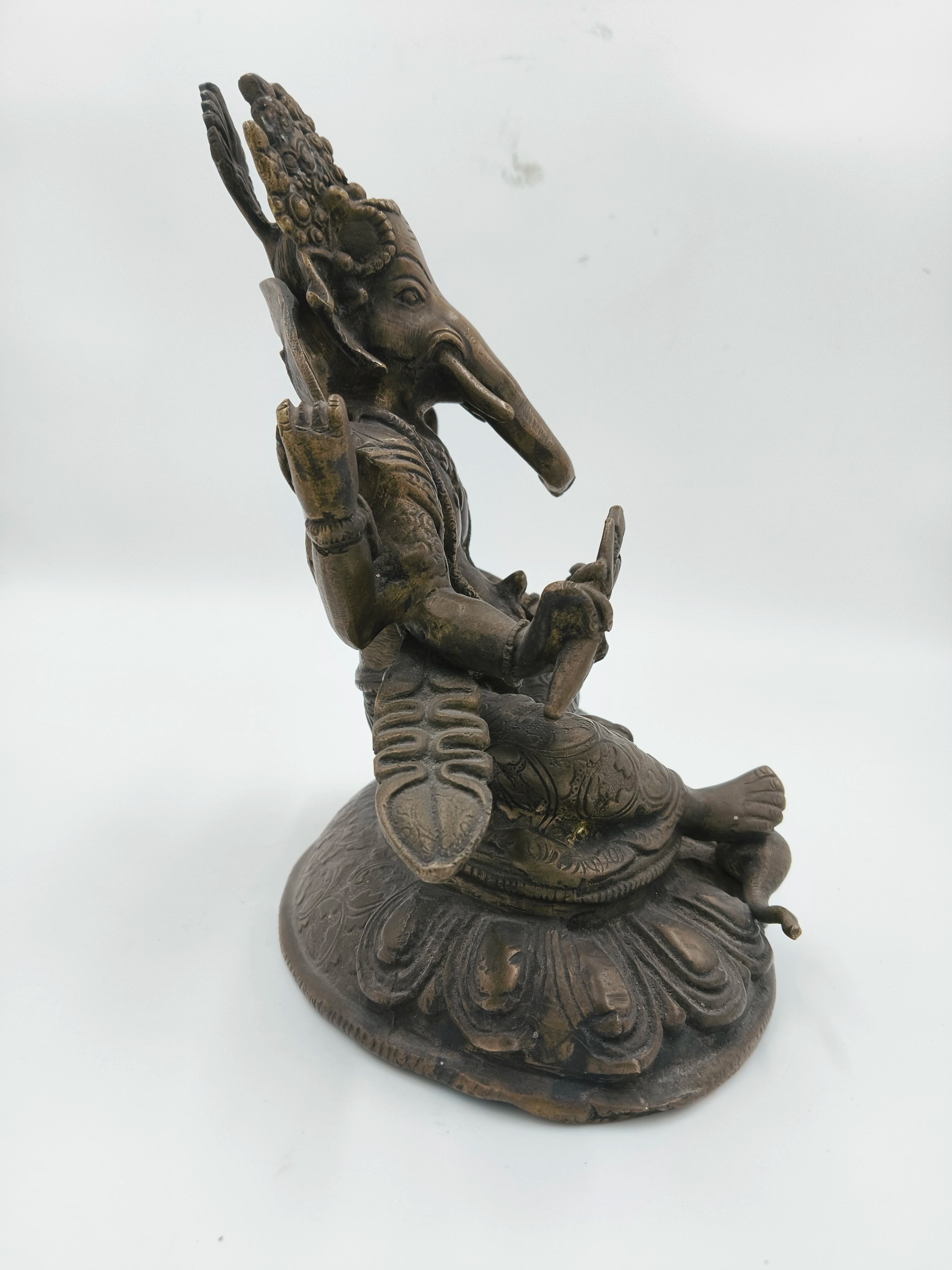 Side view of a brass Ganesh statue seated on a decorative base