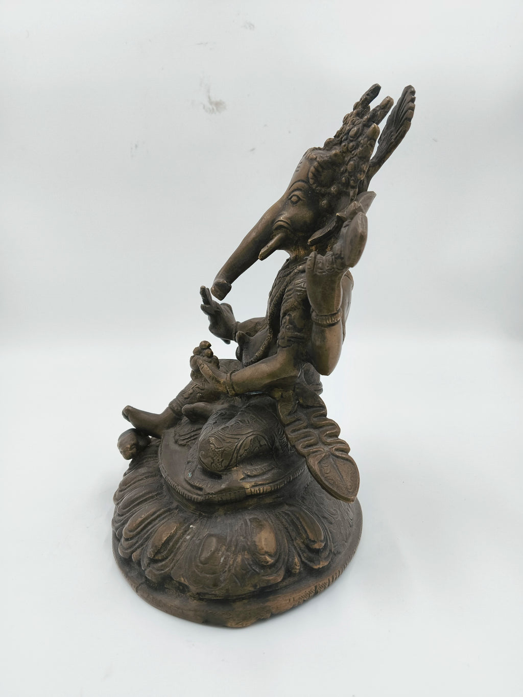 Side view of brass Ganesh statue seated on a carved base