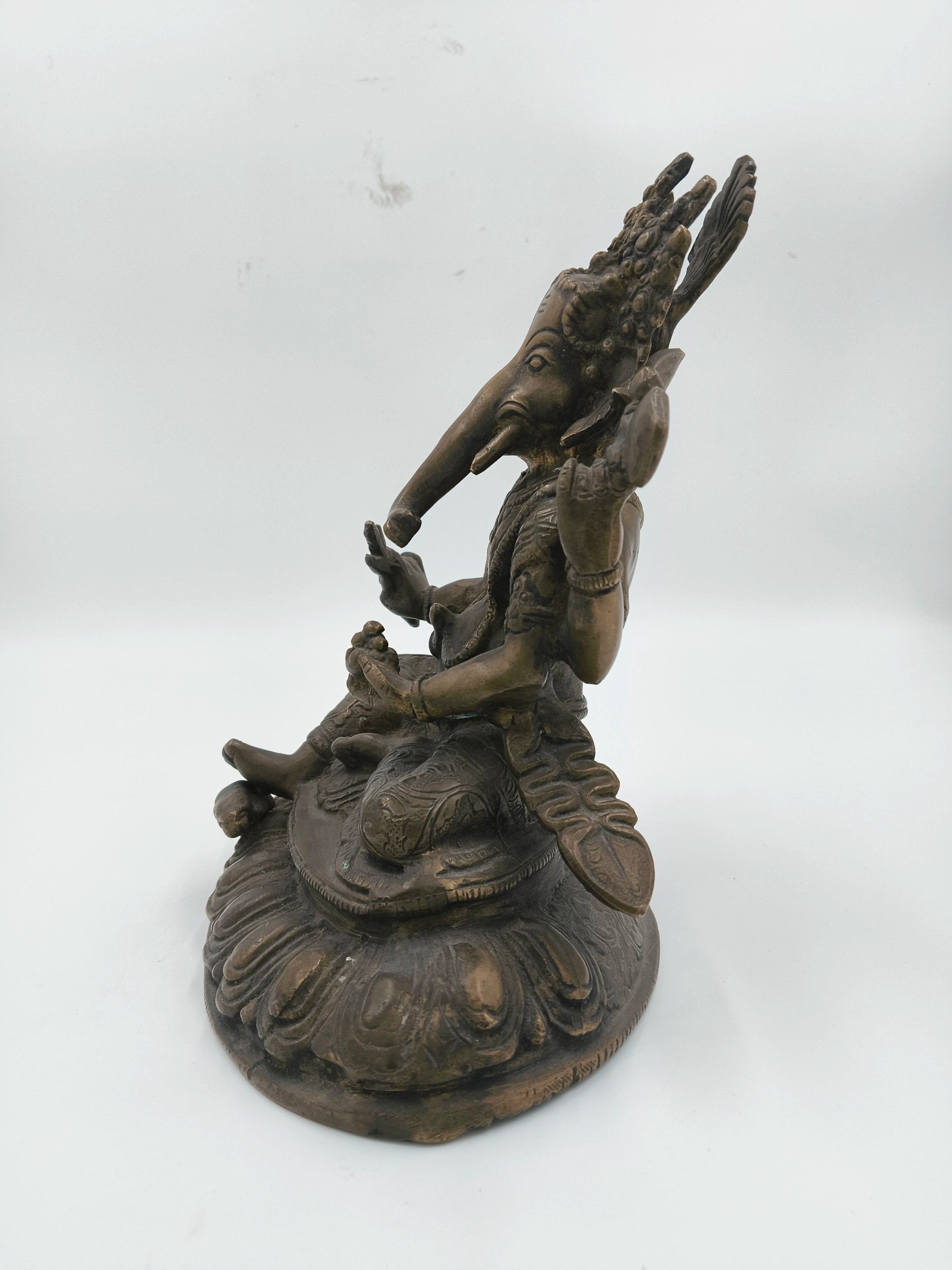 Side view of brass Ganesh statue seated on a carved base