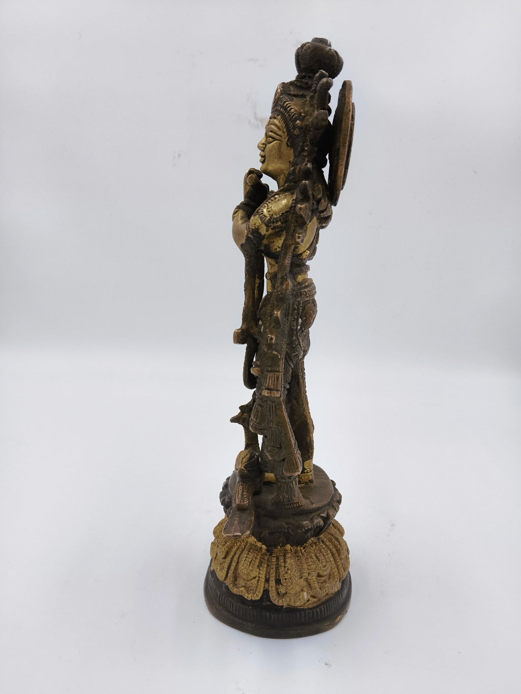 Side view of large brass Krishna statue standing on decorated base