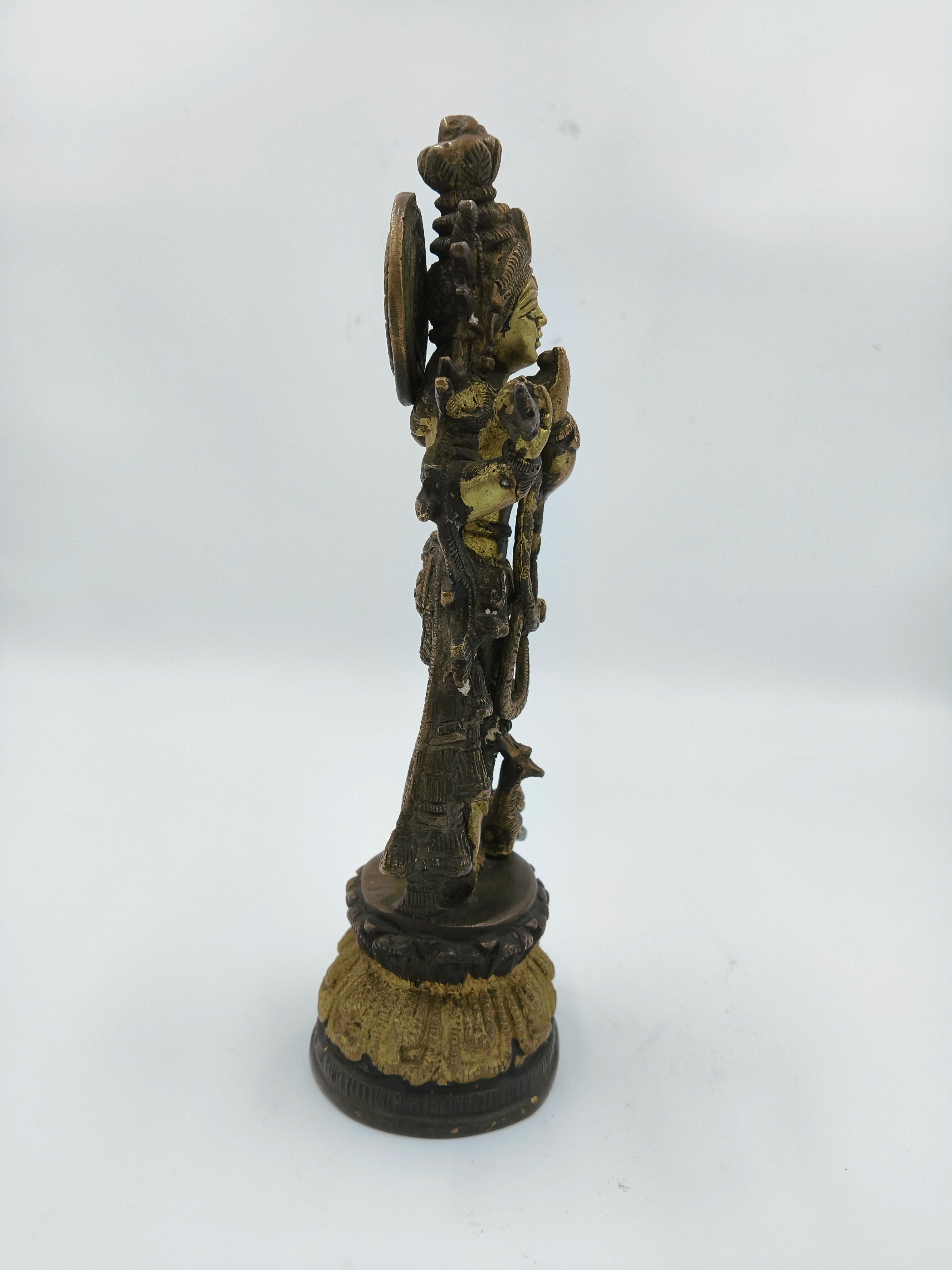 Side view of large brass Krishna sculpture on decorative base