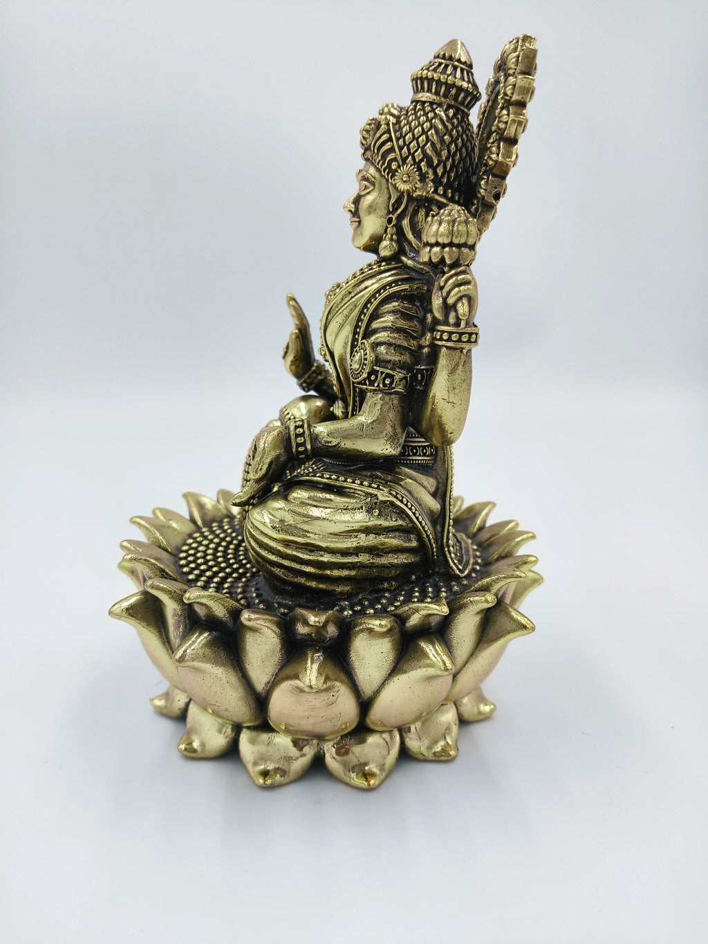 Side view of a brass statue of goddess Dhanalakshmi seated on a lotus base