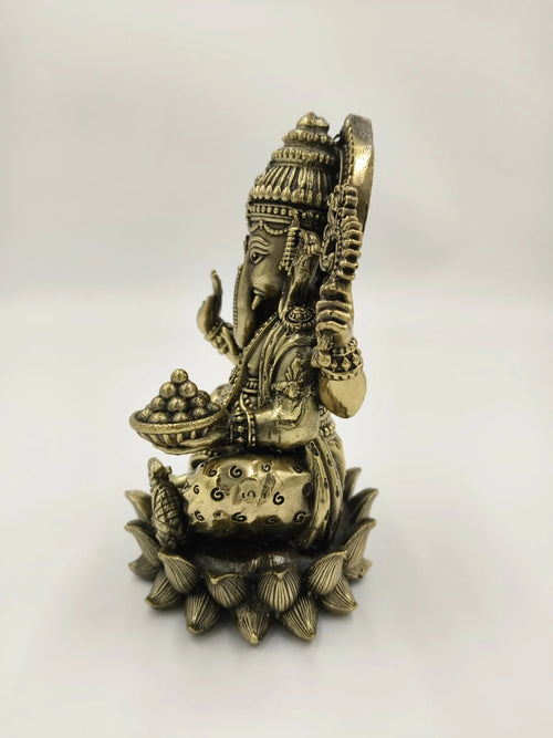 Side view of a medium brass Ganesh sitting on a lotus sculpture holding sweets