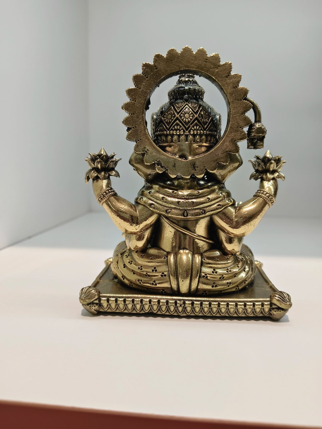 Back view of small brass Padma Hasta Ganapati statue seated on decorated base