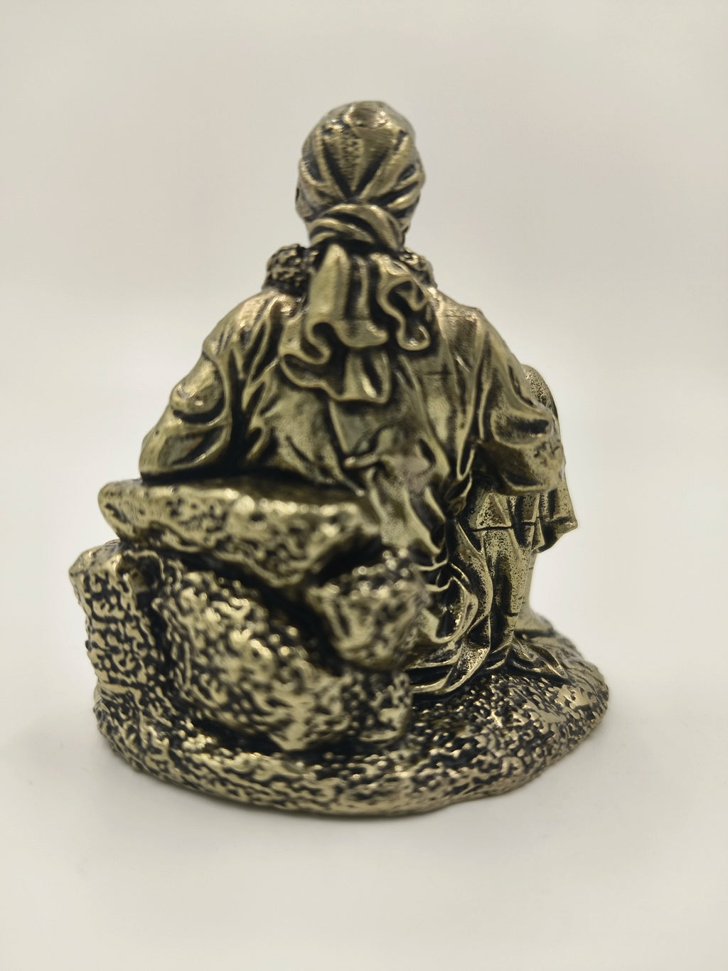 Back view of a mini brass Shirdi Sai Baba statue sitting on textured base