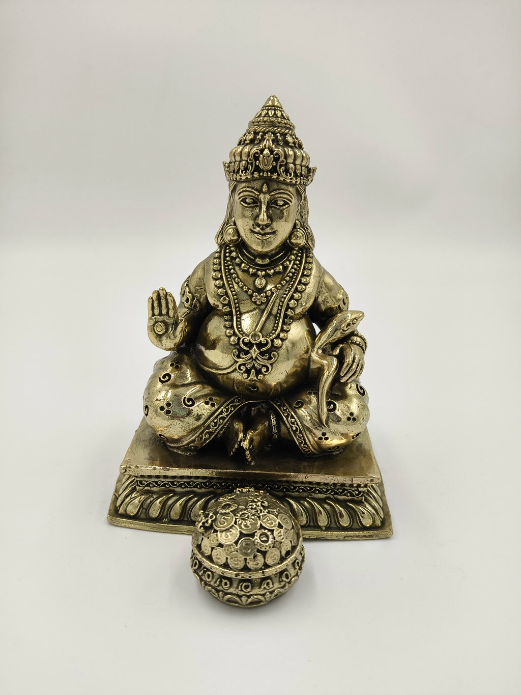 Medium brass Kubera statue seated with a spherical ornament in front