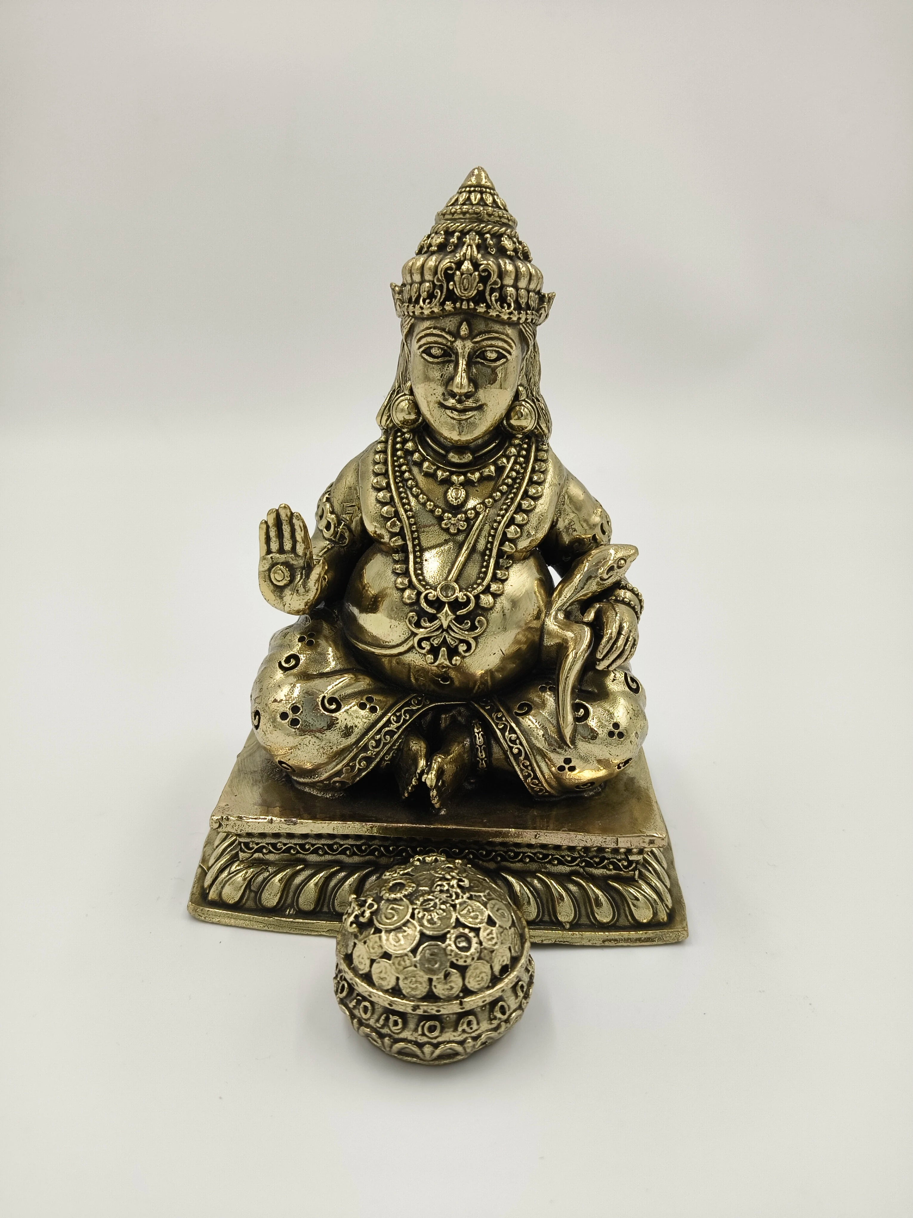 Medium brass Kubera statue seated with a spherical ornament in front