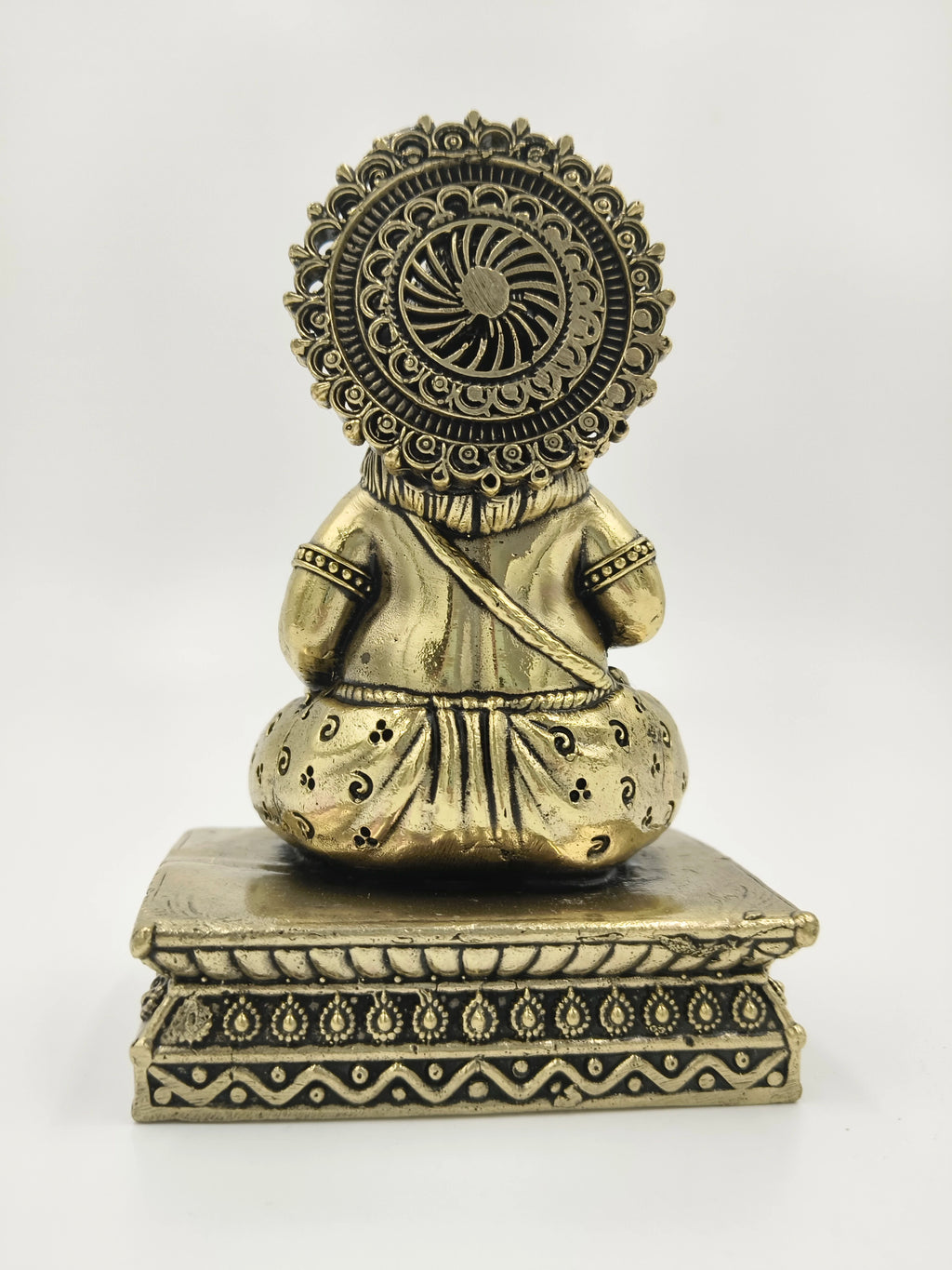 Back view of a small brass Kubera statue sitting on an ornate pedestal