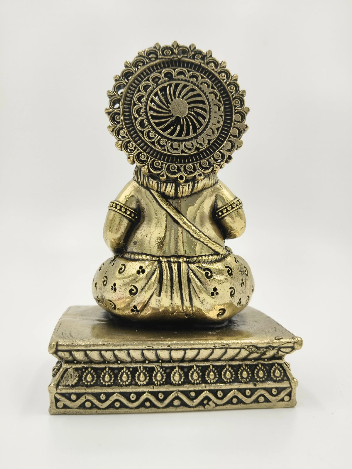 Back view of a small brass Kubera statue sitting on an ornate pedestal