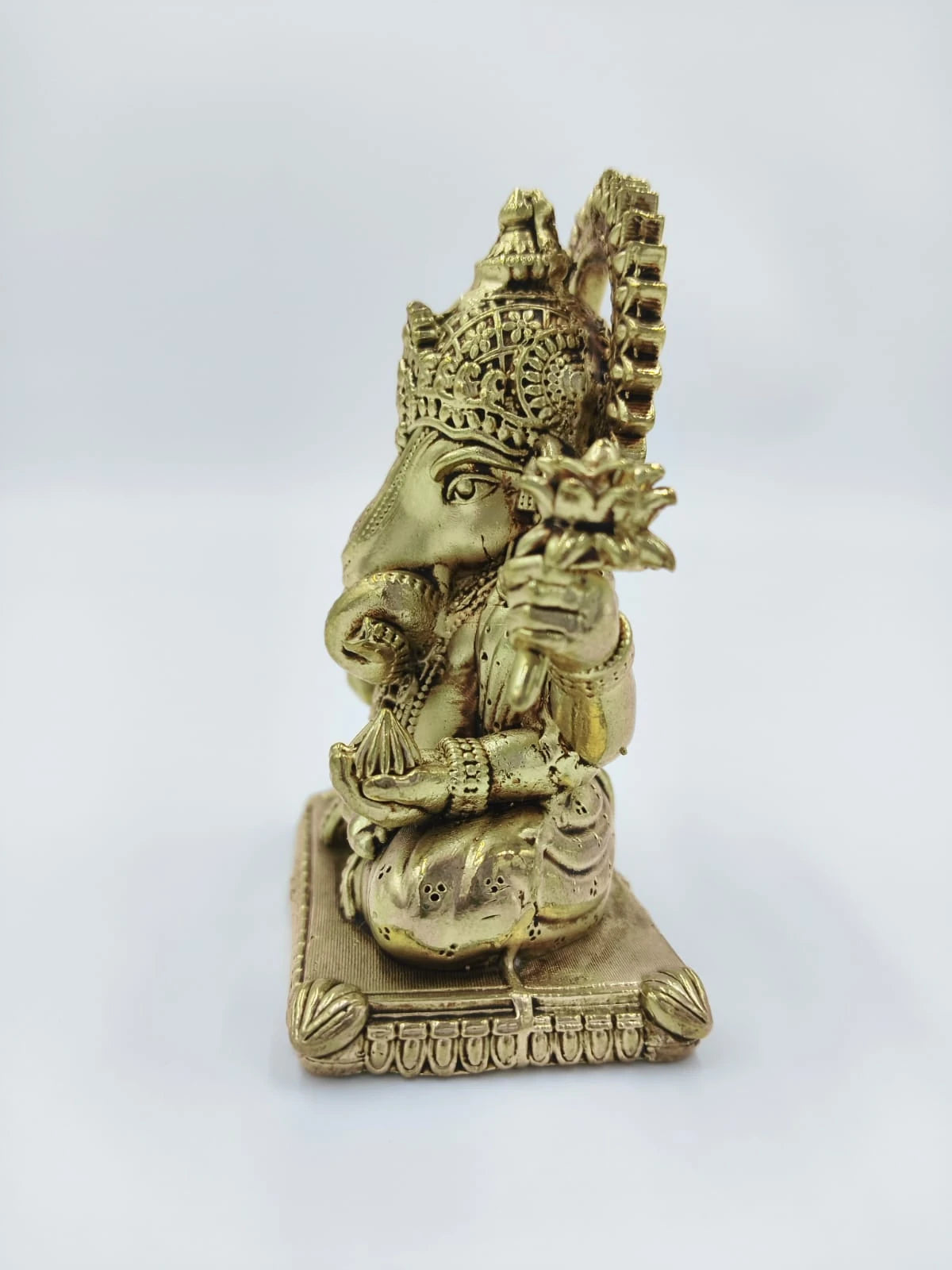 Side view of a small brass Padma Hasta Ganapati sculpture sitting on a decorative base