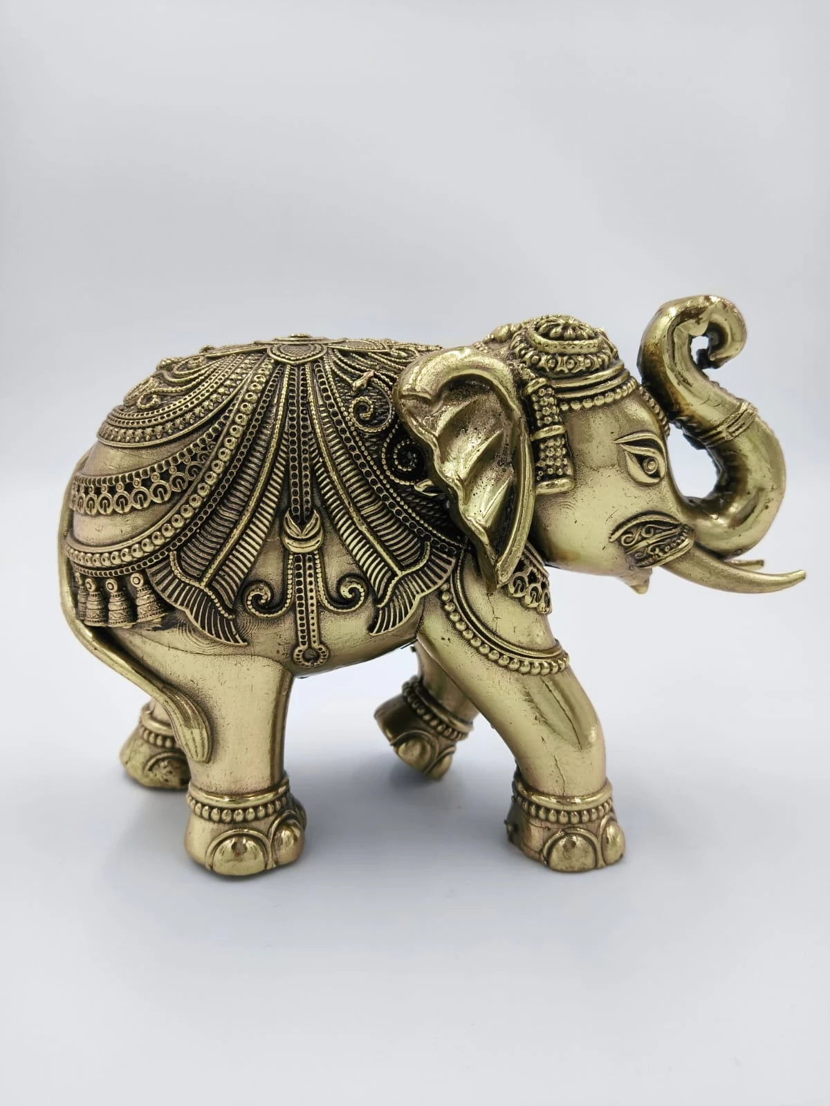 Small brass elephant figurine with detailed ornamental carvings side view