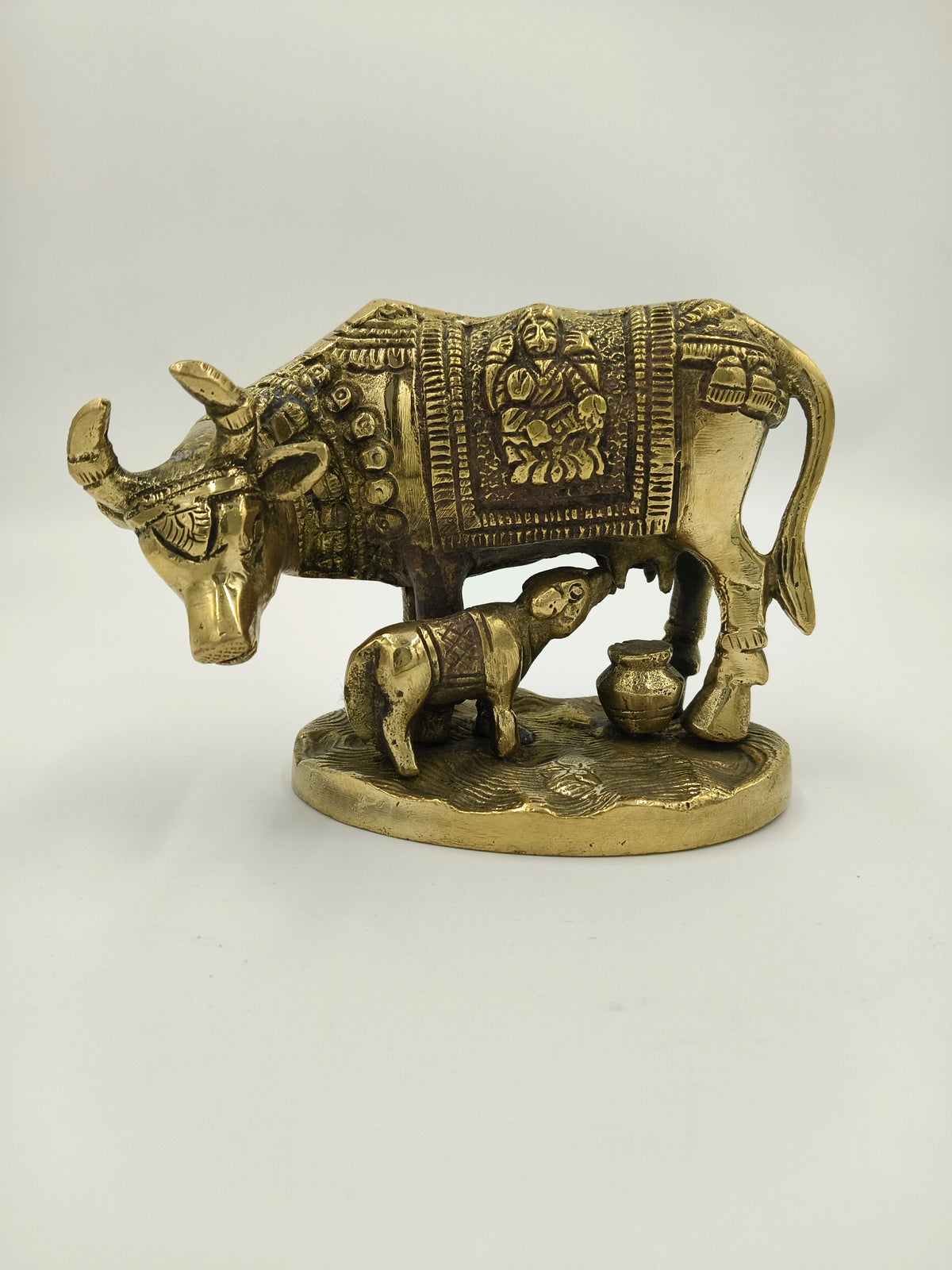 Brass cow and calf idol with intricate carvings and a pot on a flat base