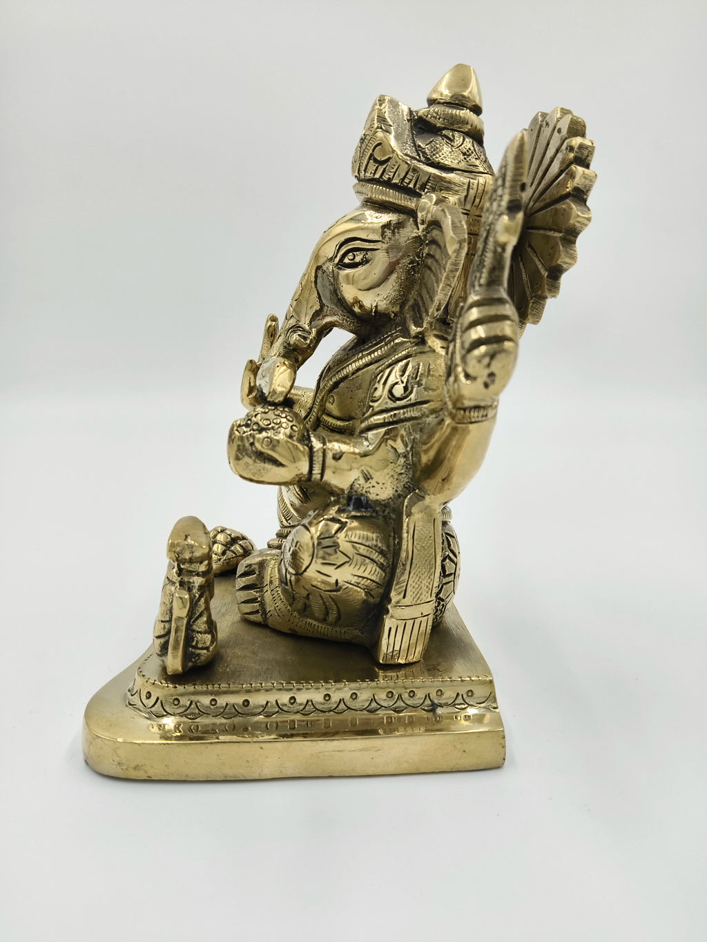 Large brass Raja Ganapati statue sitting on a decorative base, side view