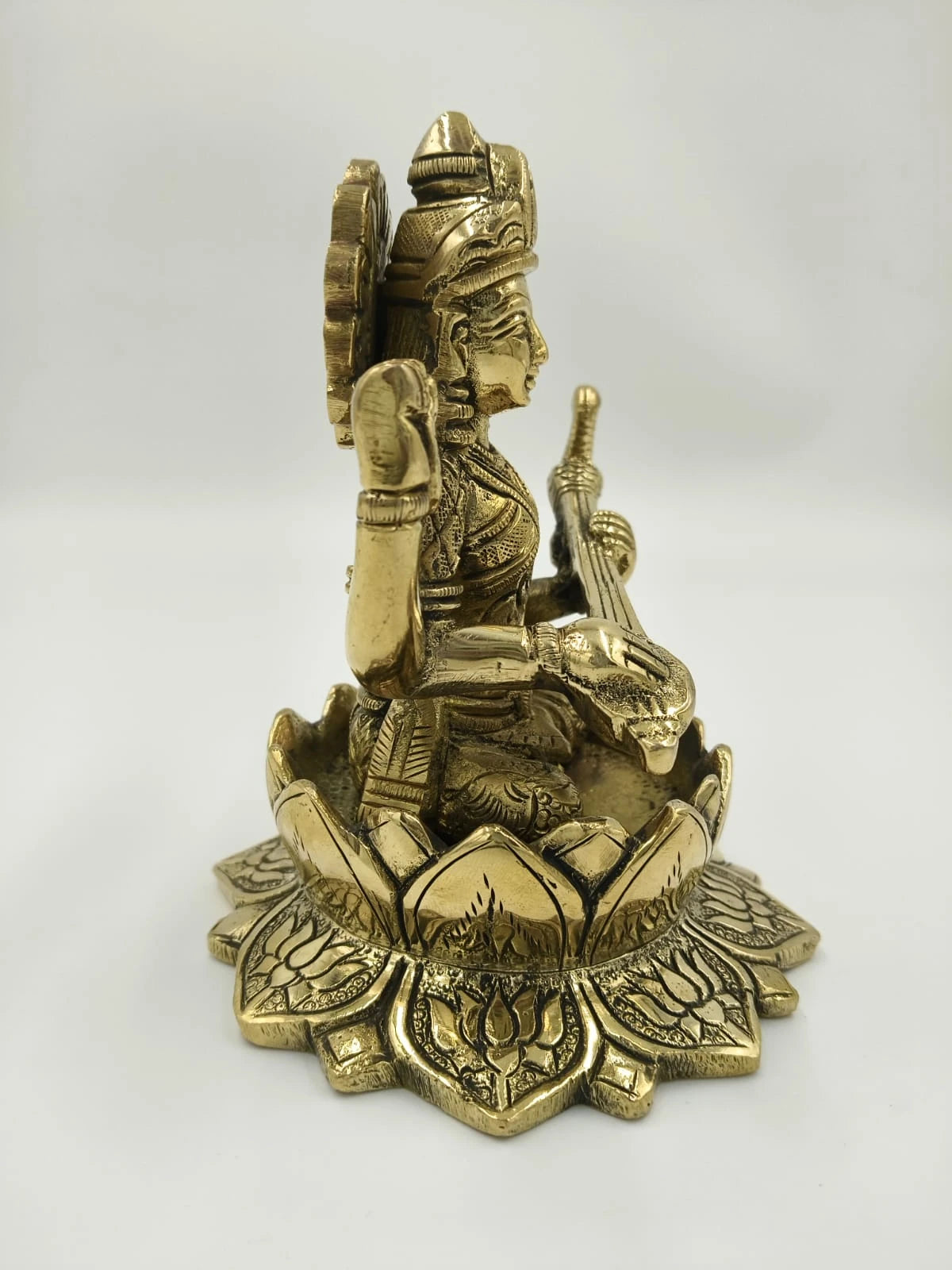 Side view of brass Saraswathi statue seated on lotus base holding veena