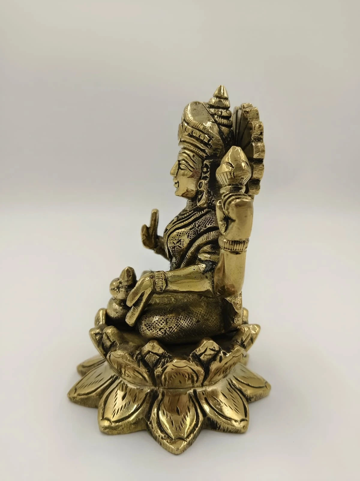 Side view of a medium brass Lakshmi sculpture seated on a lotus base