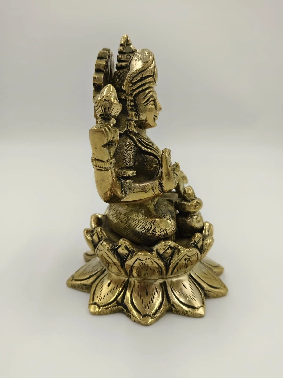 Side view of a medium brass sculpture of Lakshmi seated on a lotus