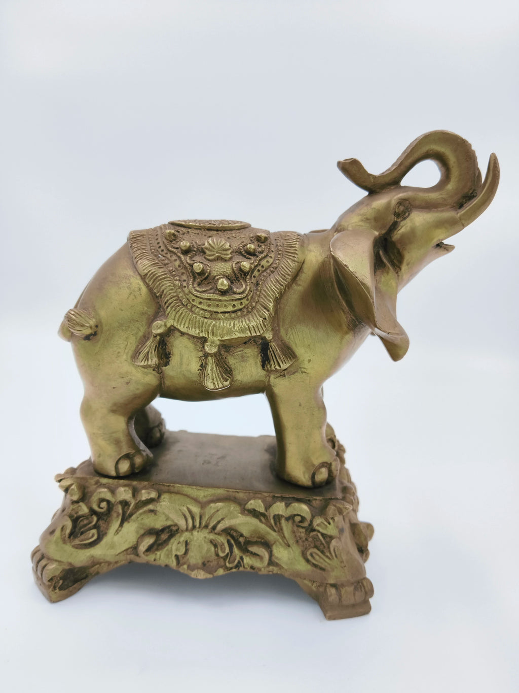 Brass elephant sculpture with decorative saddle on ornate base, side view